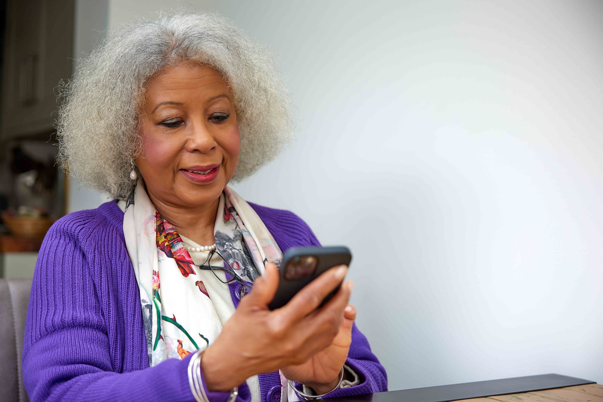 An older woman is sitting at a table looking at her cell phone.