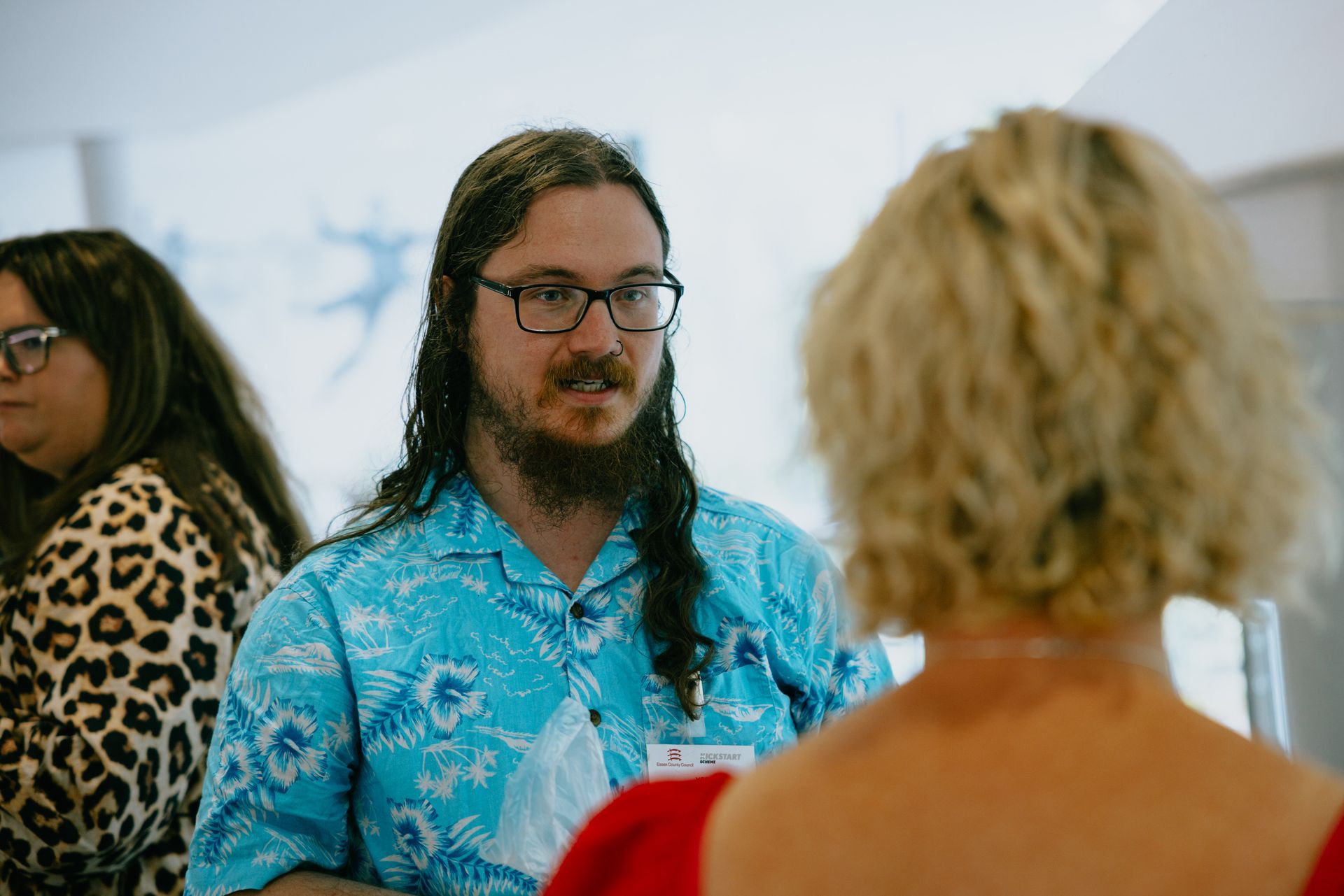 A man with long hair and glasses is talking to a woman.