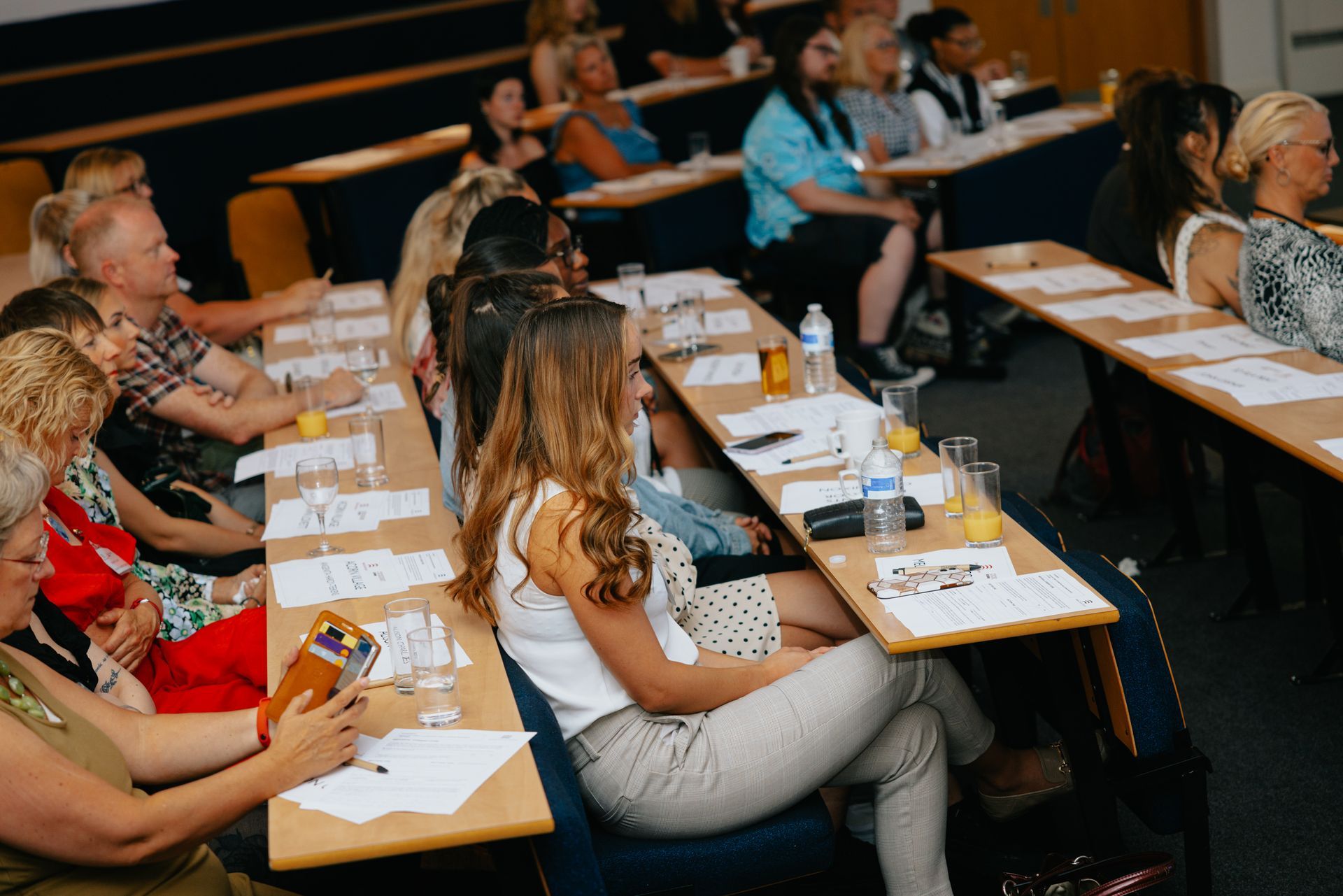 A group of people are sitting at long tables in a classroom.