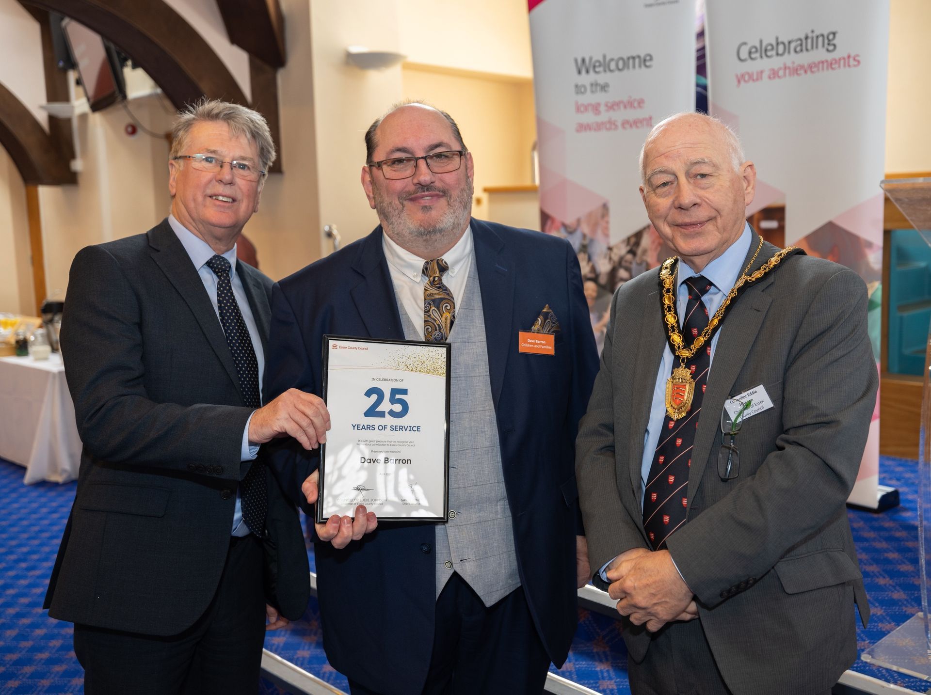 Three men in suits are standing next to each other holding a sign that says 25.