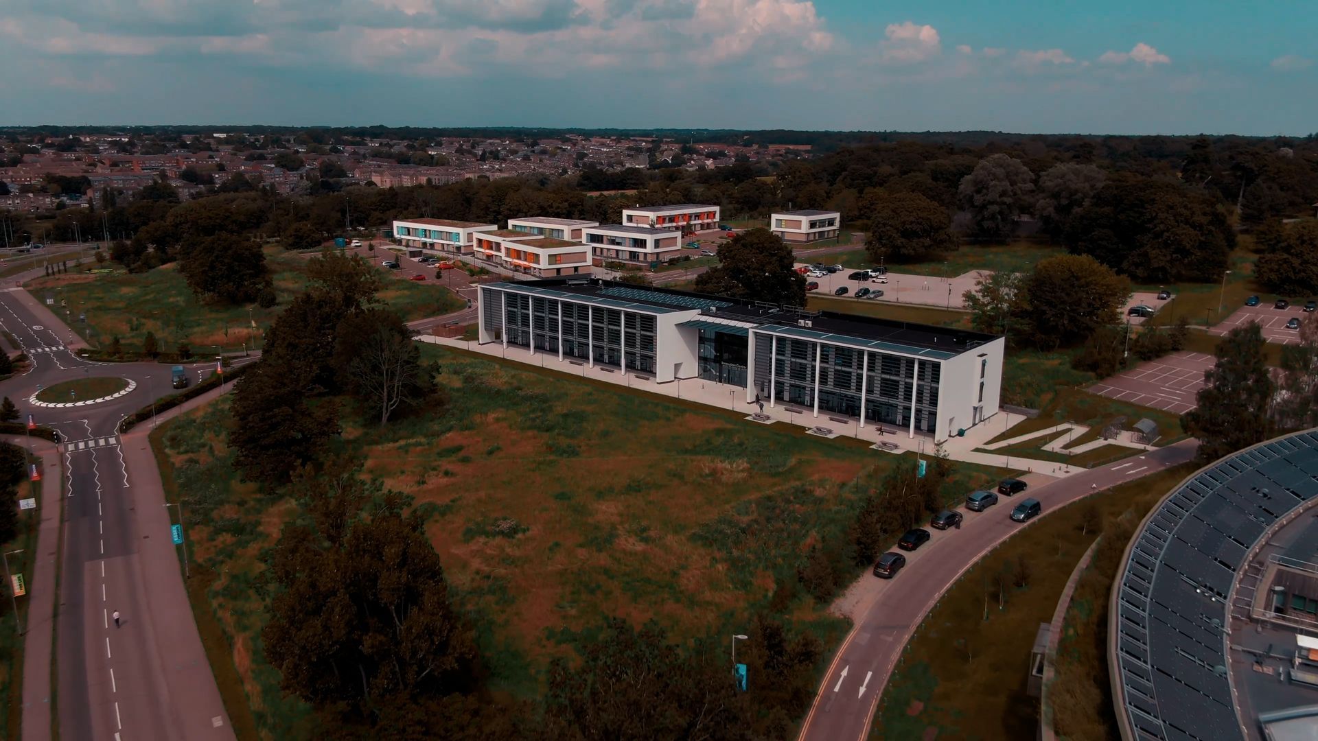 An aerial view of a large building surrounded by trees and a road.