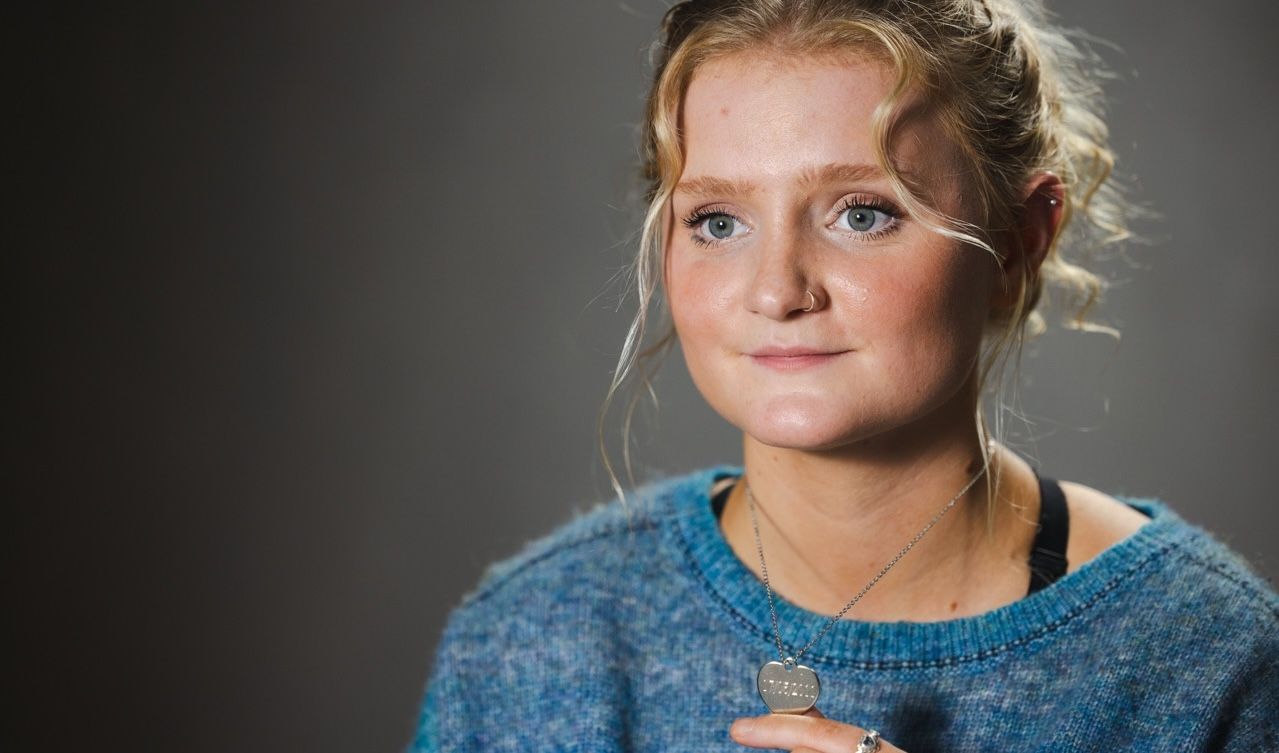 A young woman is wearing a blue sweater and a necklace.