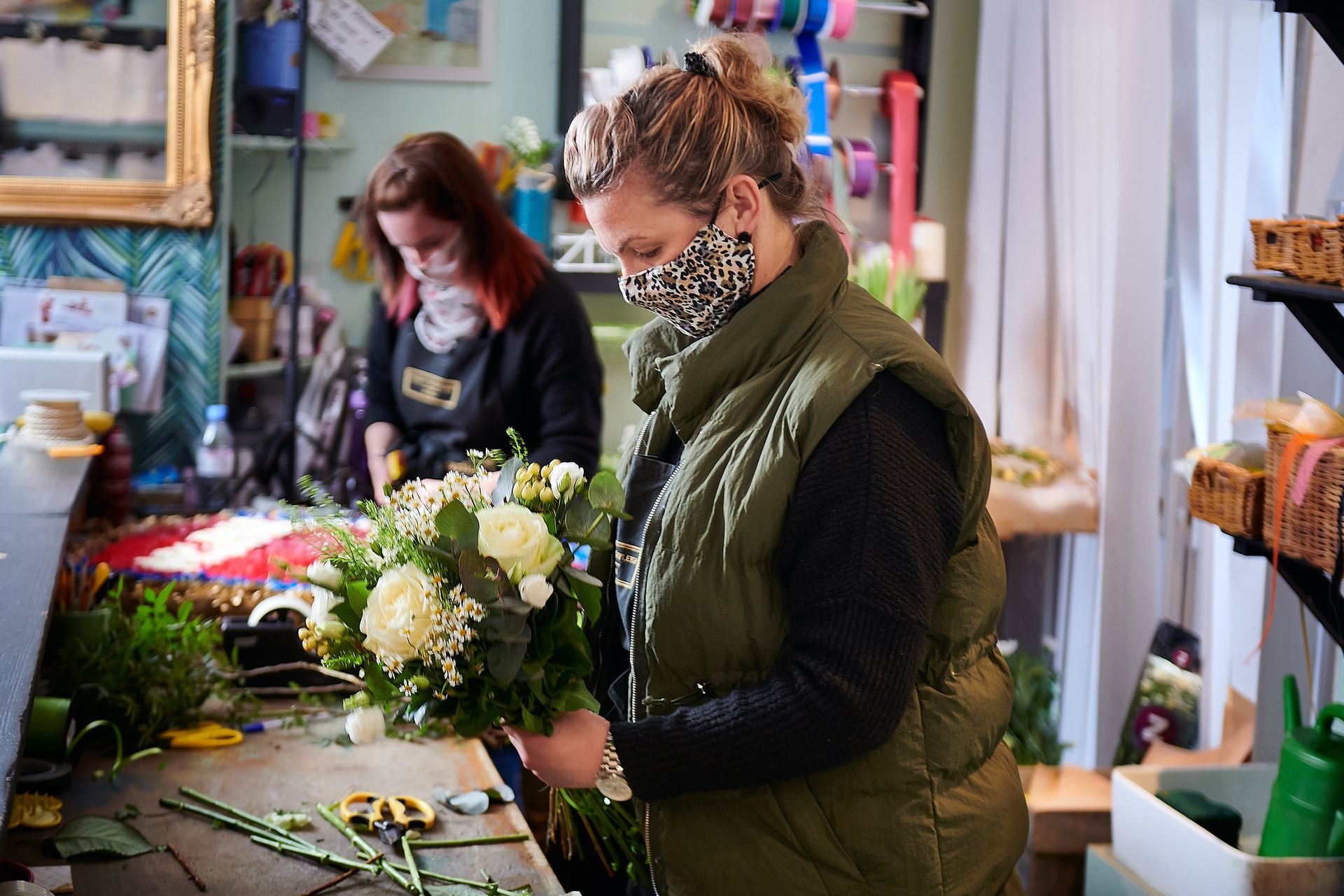 A woman wearing a mask is making a bouquet of flowers in a flower shop.