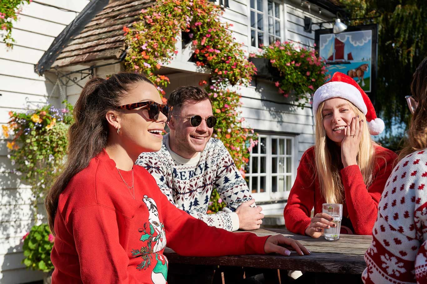 A group of people wearing christmas sweaters are sitting at a table.