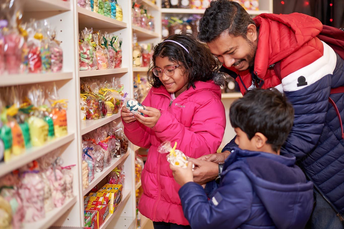 A man and two children are looking at candy in a store.