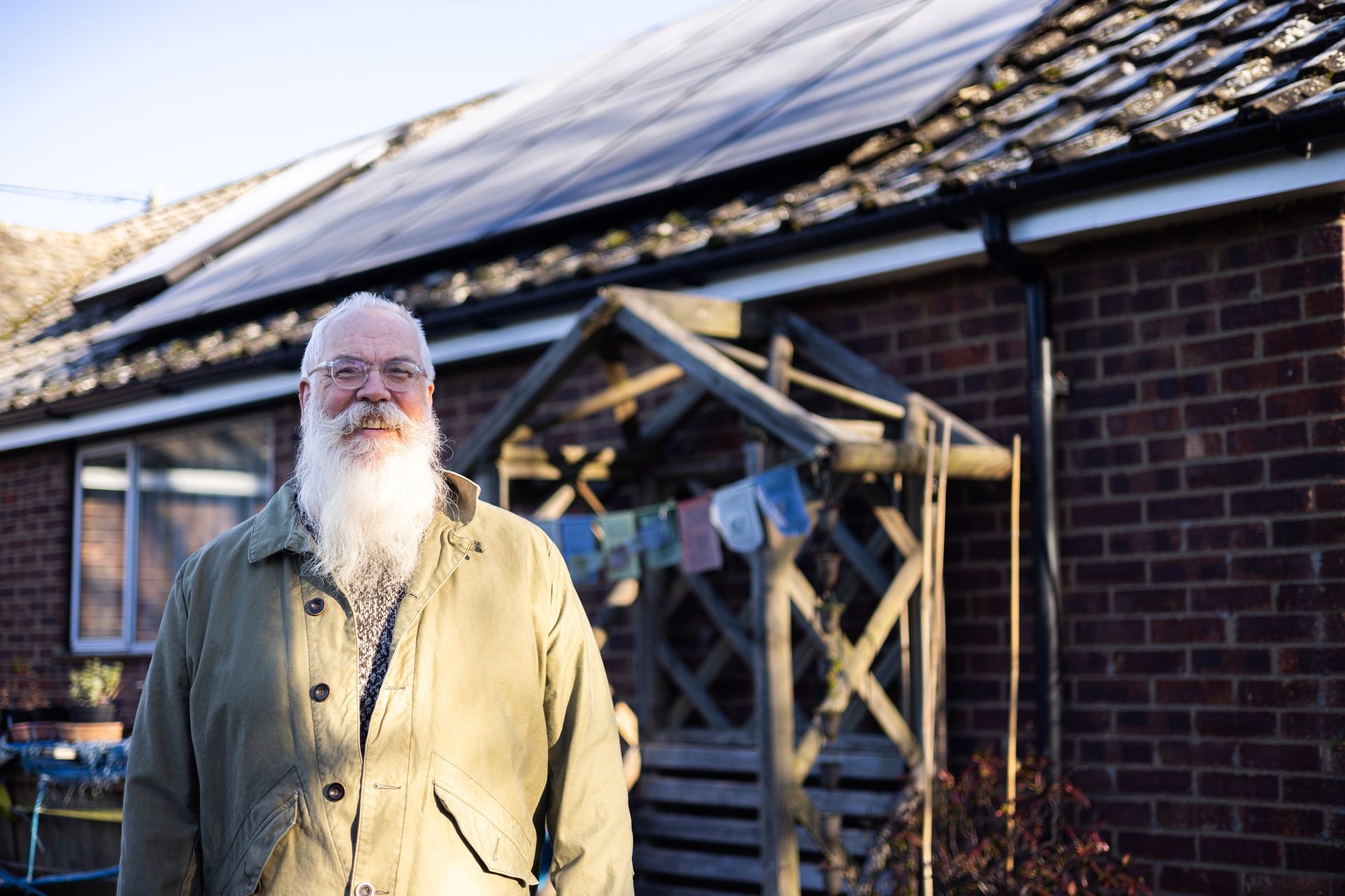 A man with a beard is standing in front of a brick house.