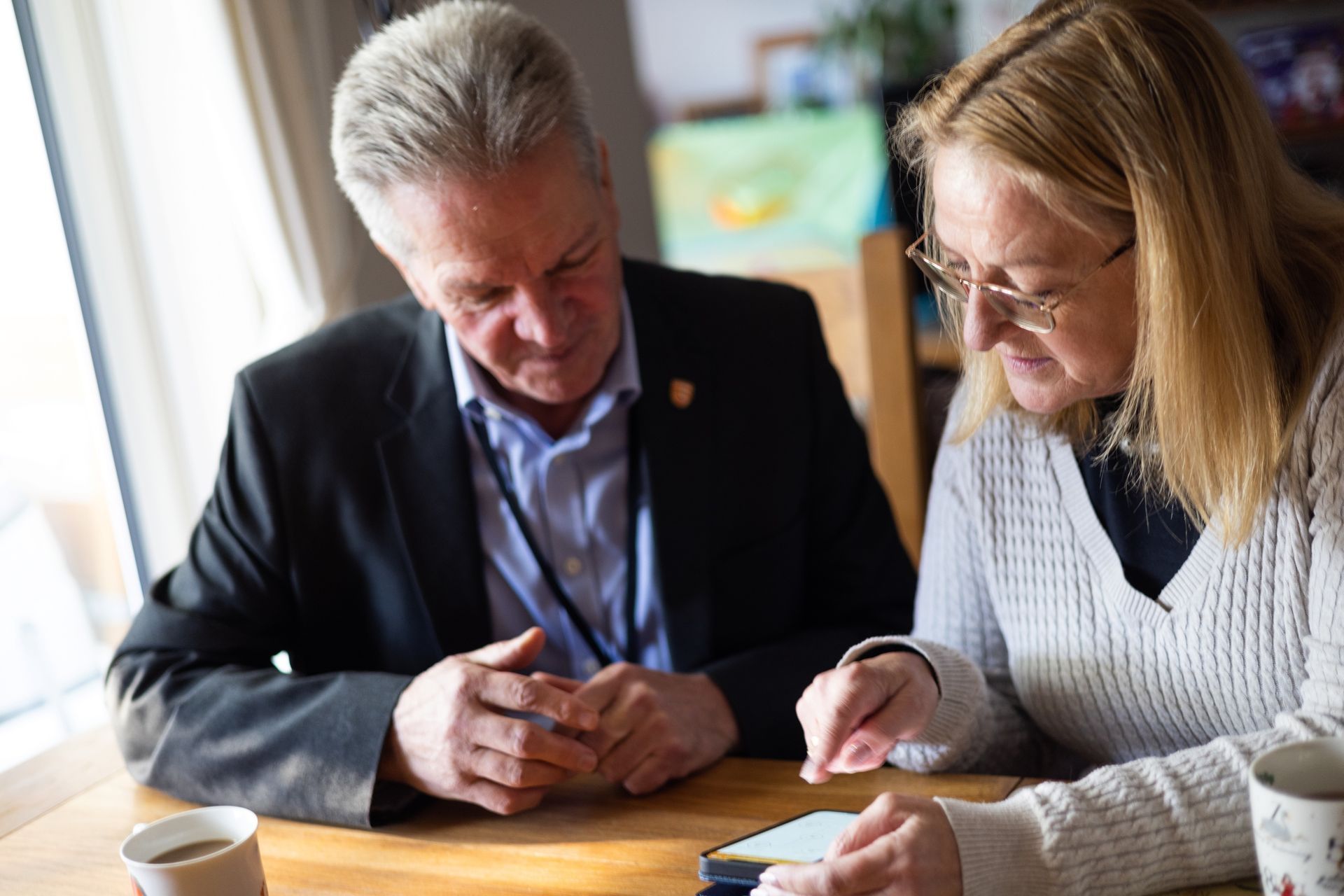 A man and a woman are sitting at a table looking at a cell phone.