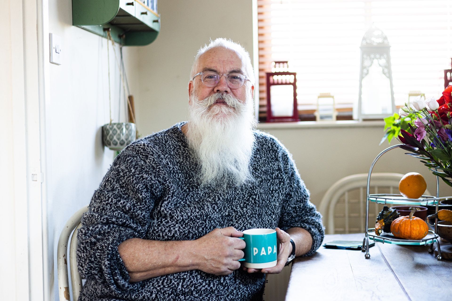 A man with a beard is sitting at a table holding a cup of coffee.