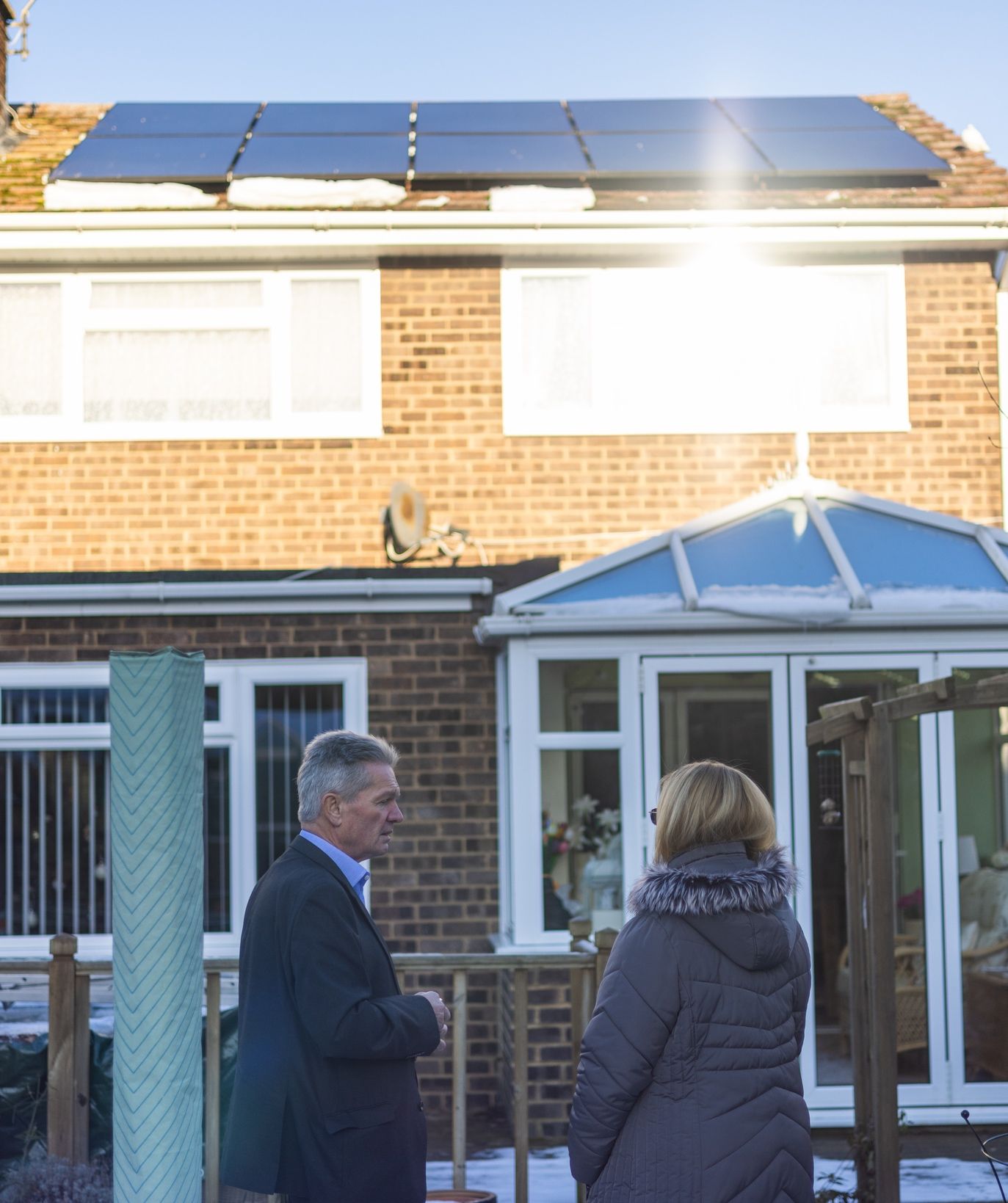 A man and a woman are standing in front of a house with solar panels on the roof