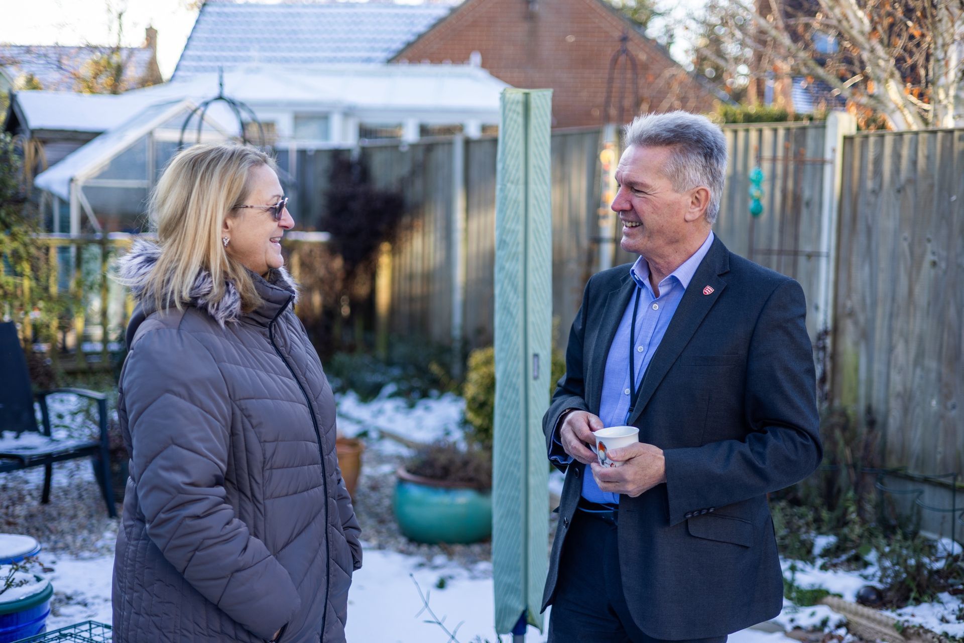 A man and a woman are standing in the snow talking to each other.
