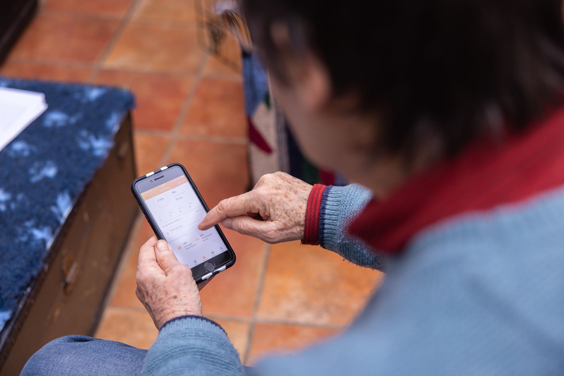 An elderly woman is using a smart phone while sitting on a couch.
