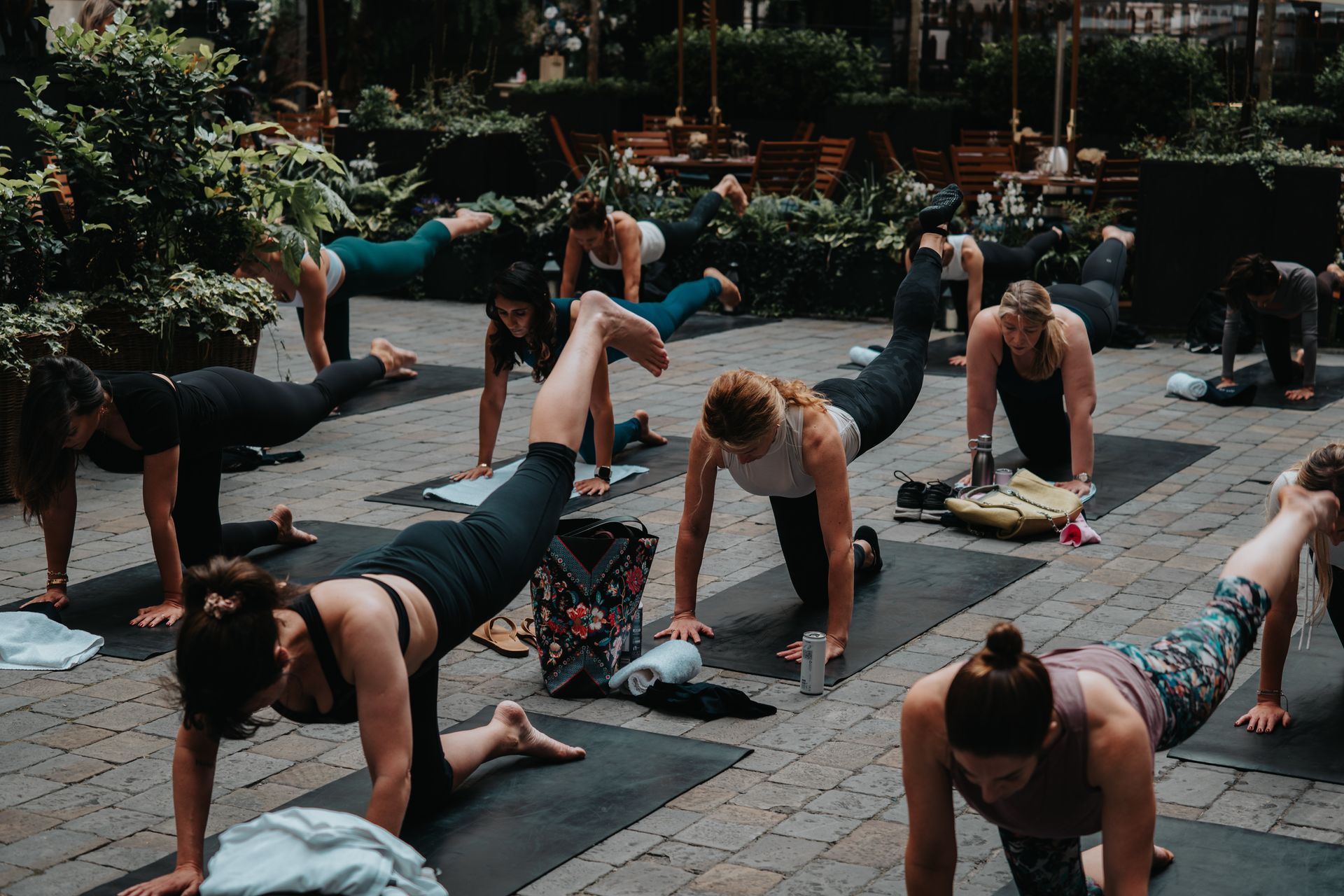 A group of women are doing yoga exercises on yoga mats outside.