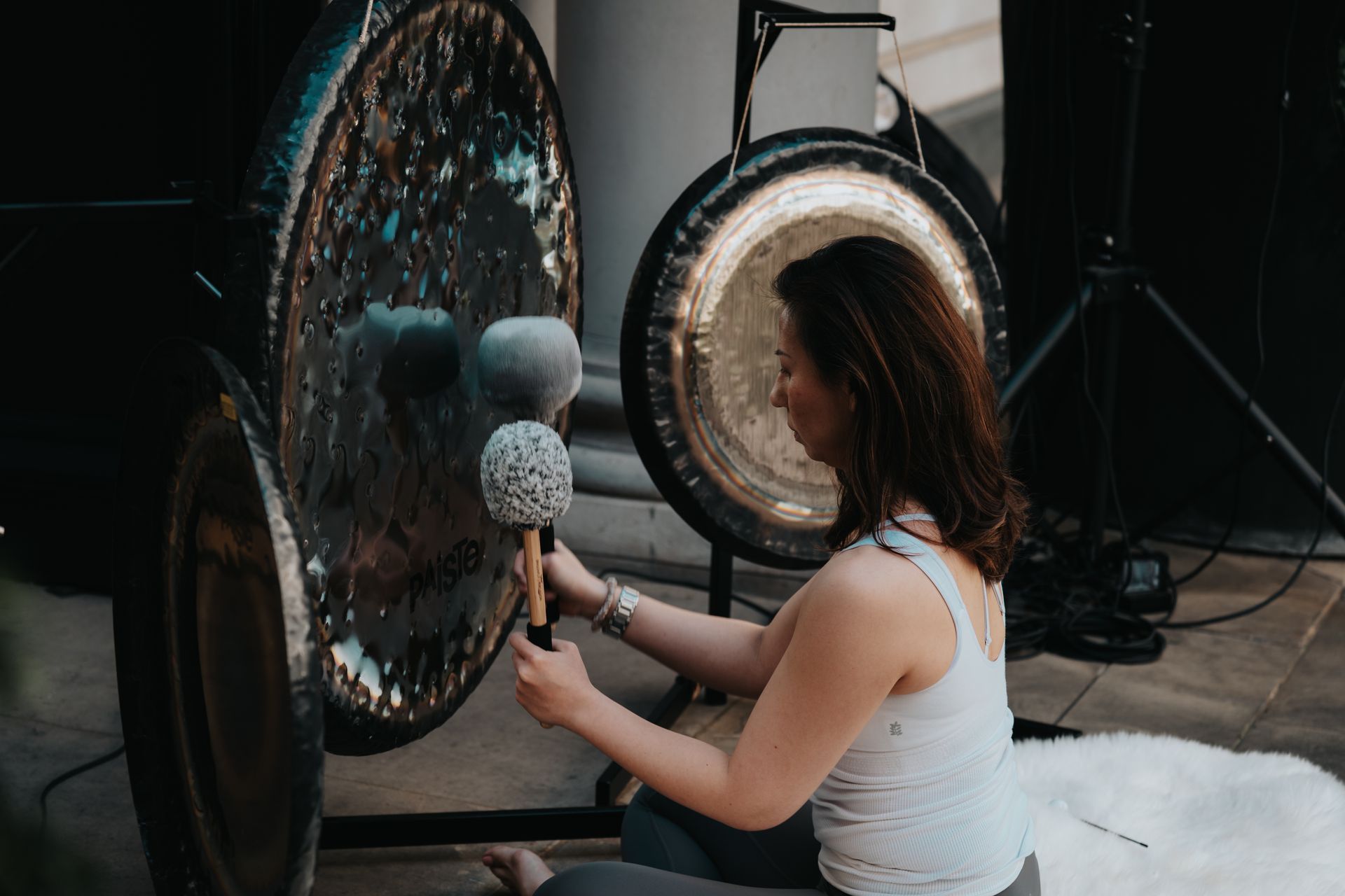 A woman is sitting on the floor playing a gong.