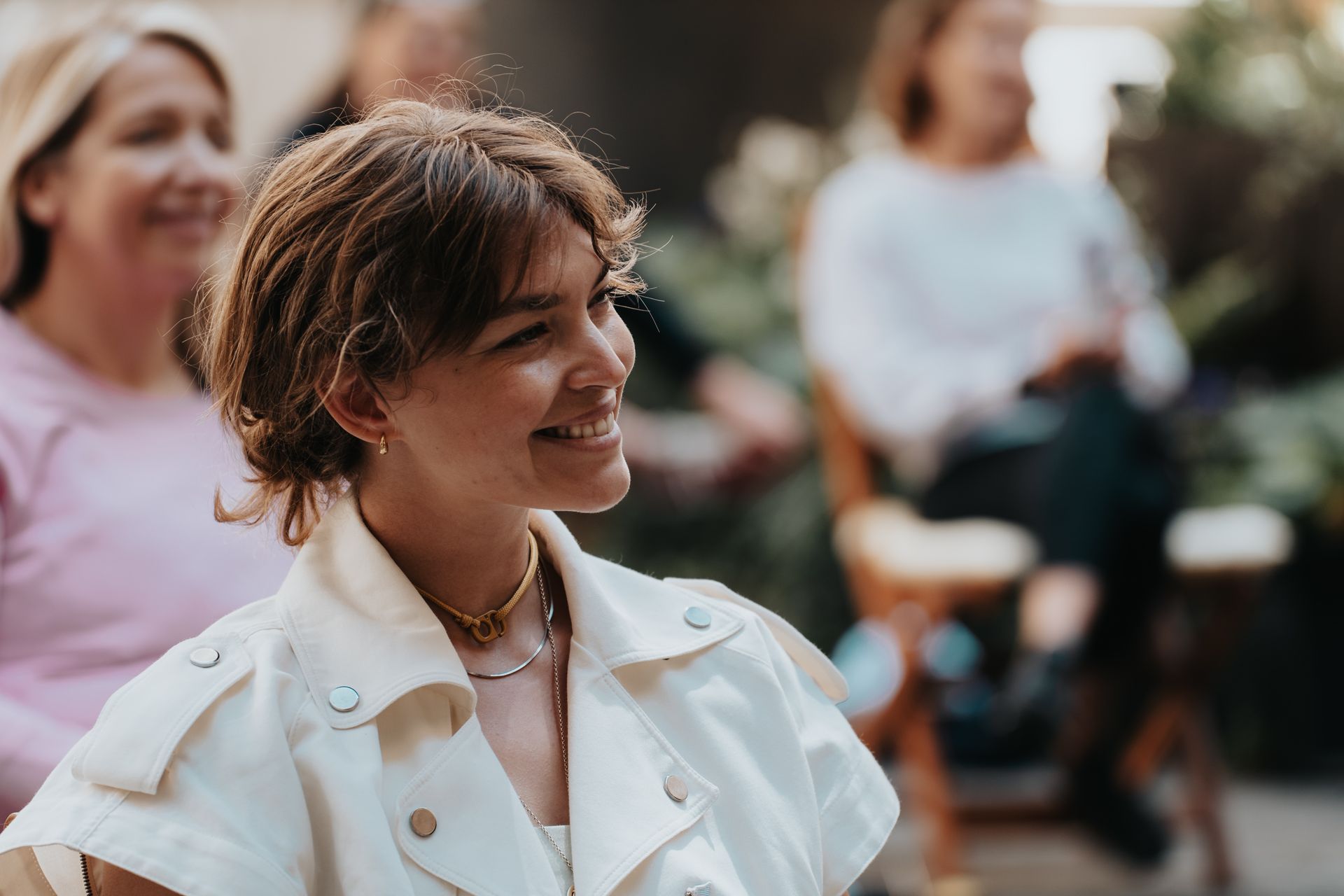 A woman in a white jacket is smiling while sitting in a chair.