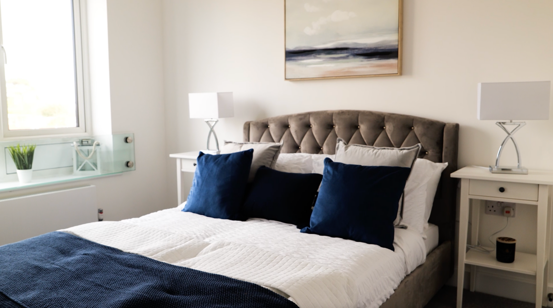 A bedroom with a bed , nightstand , lamps and a painting on the wall.