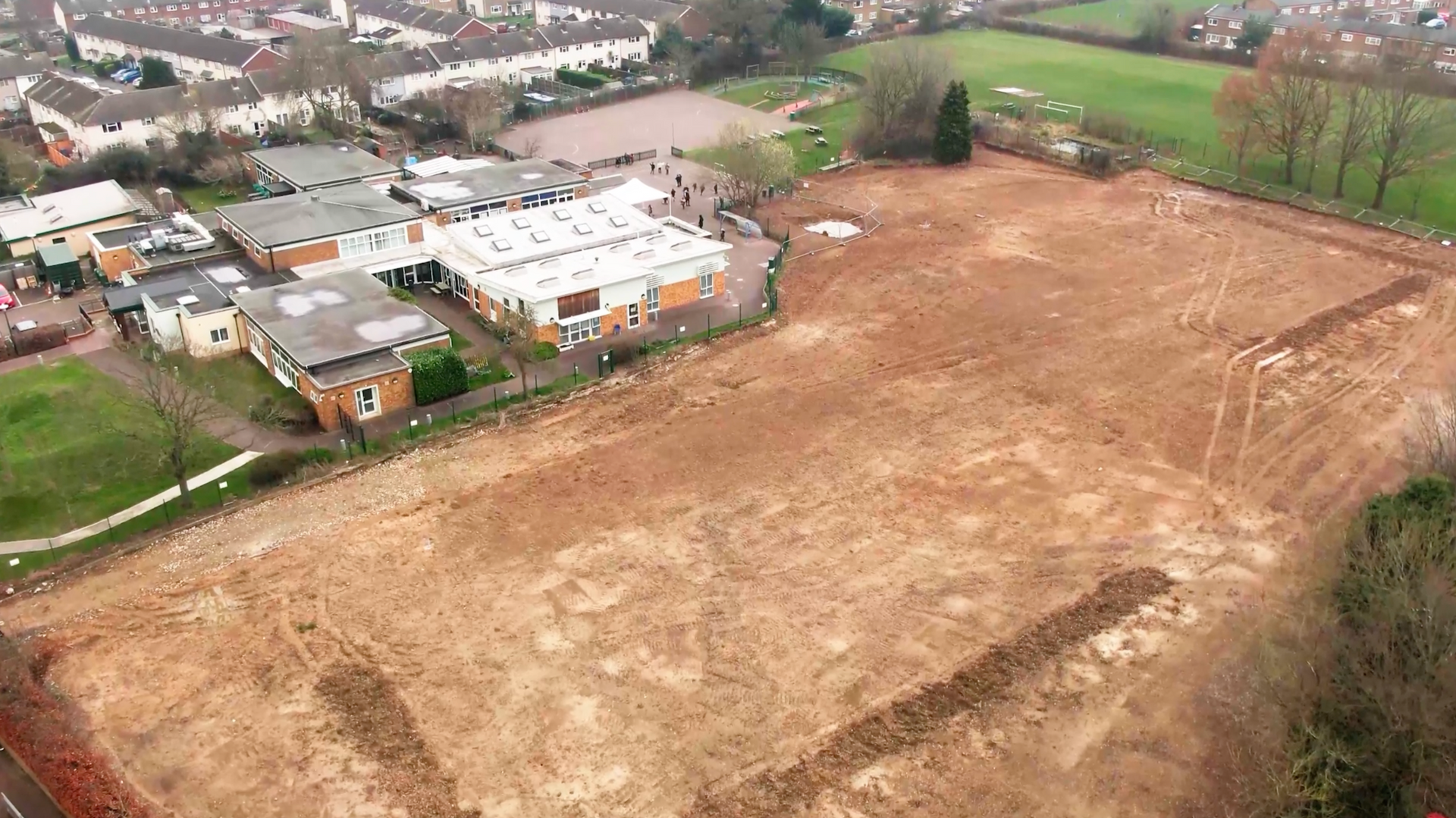 An aerial view of a large dirt field with houses in the background.