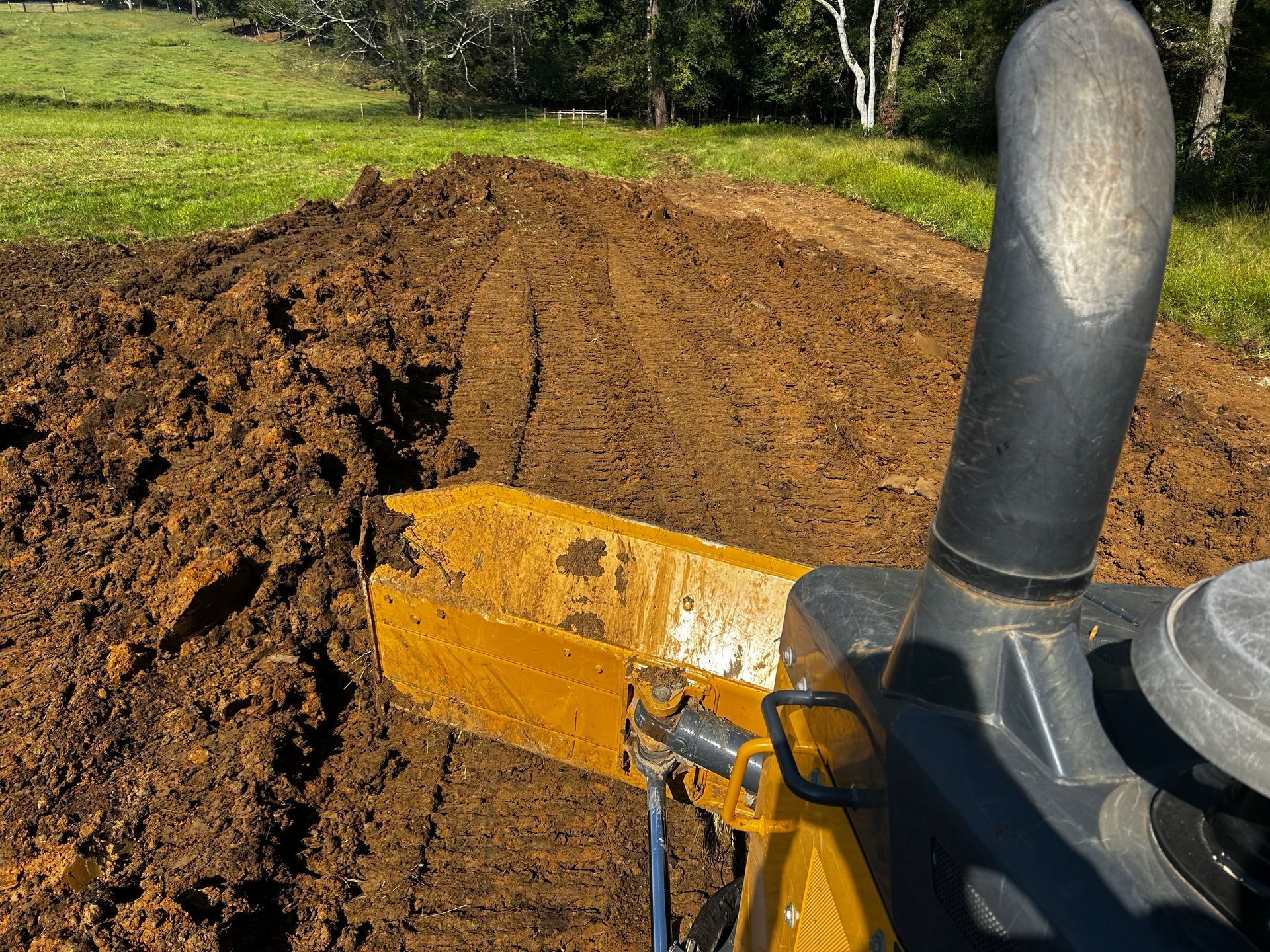 Yellow bulldozer blade pushing dirt in a grassy field