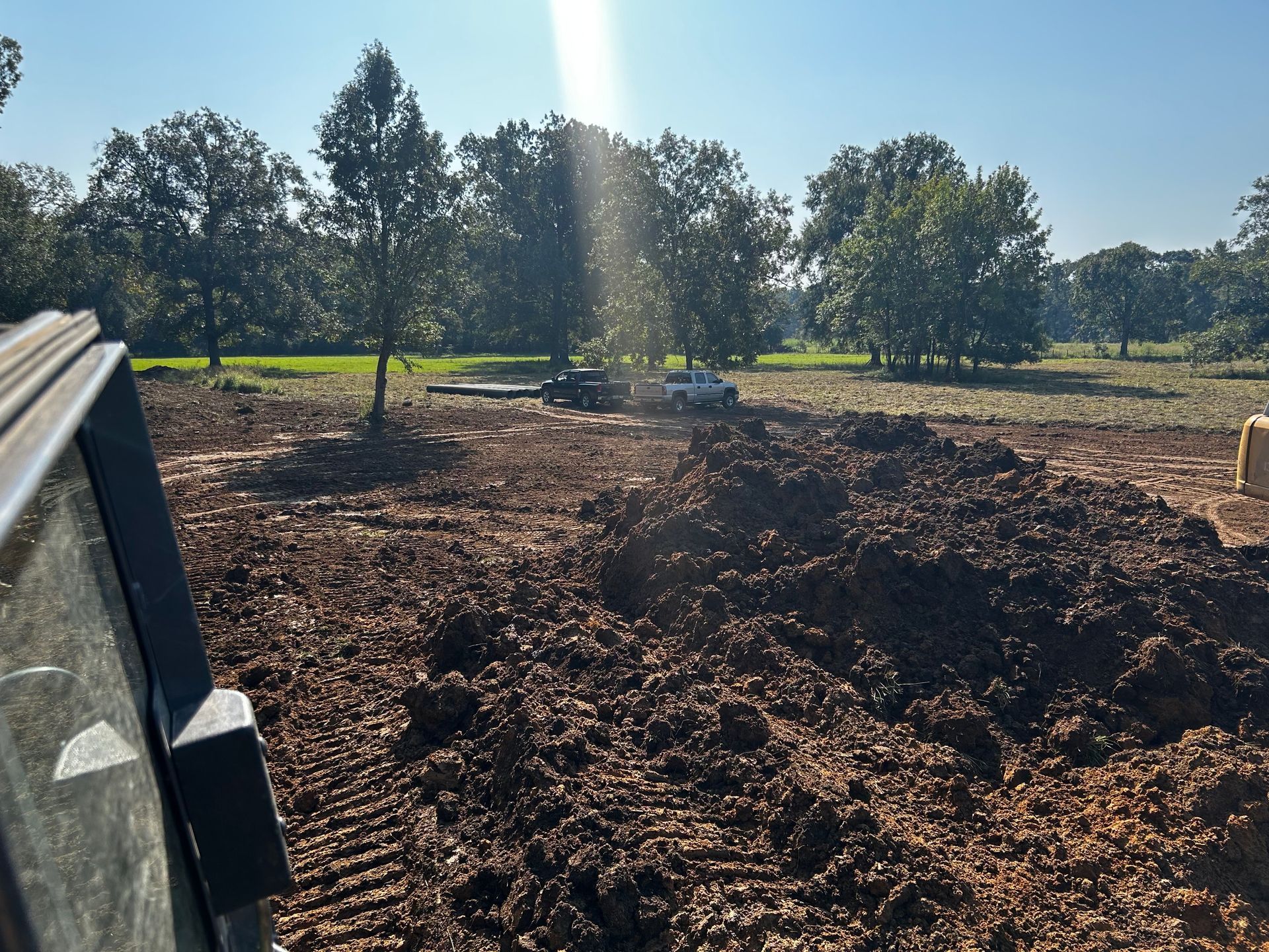 Cleared dirt lot with trees in the background and sunlight streaming over the field