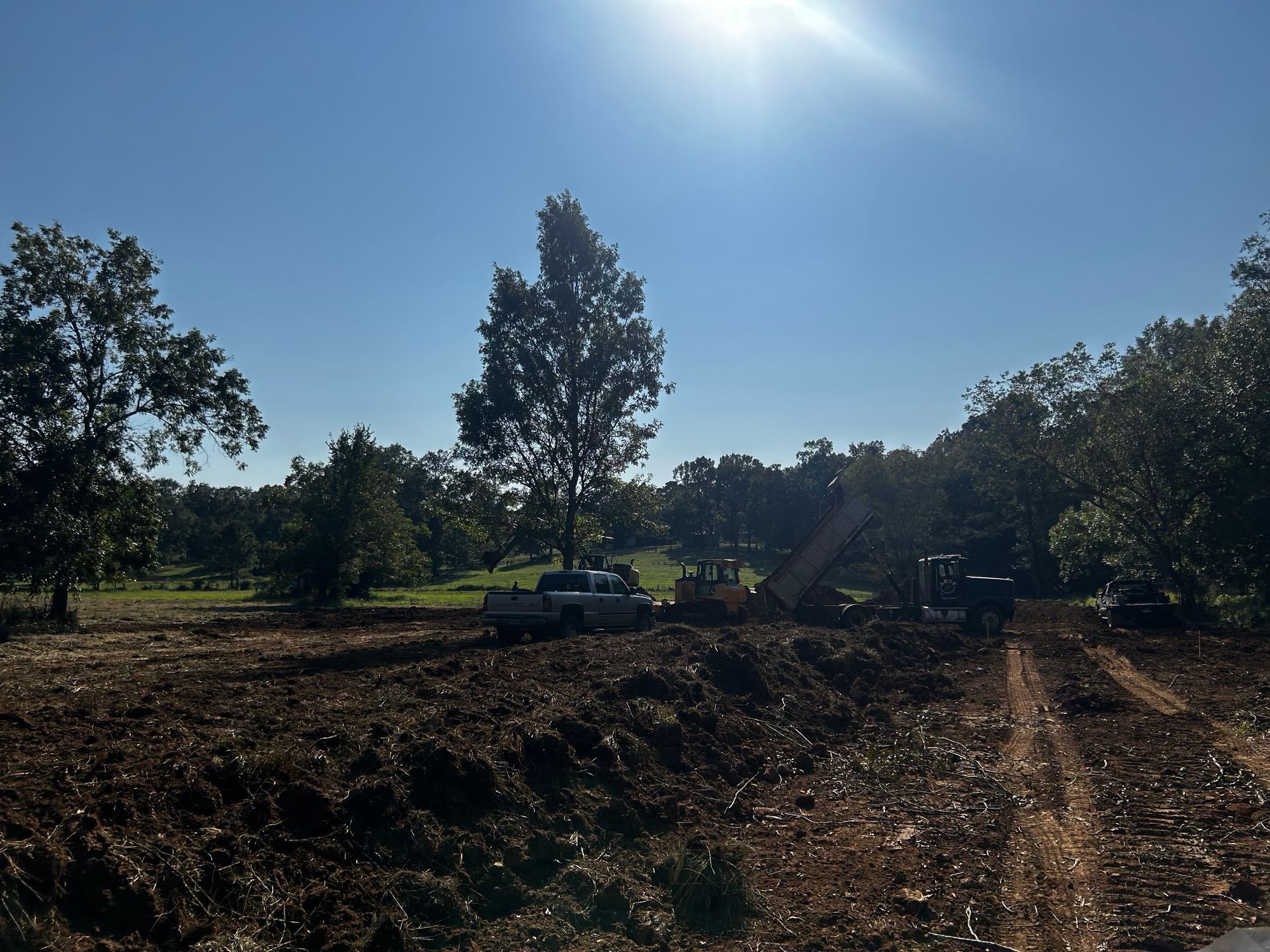 Sunny rural dirt road with trees, a parked vehicle, and dug earth under a bright blue sky