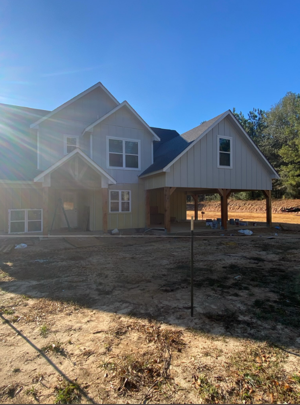 Two-story house with gray siding and covered porch on a sunny, bare lot