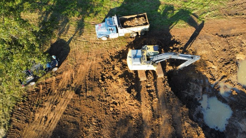 Two excavators working on a muddy dirt site near a water-filled pit.