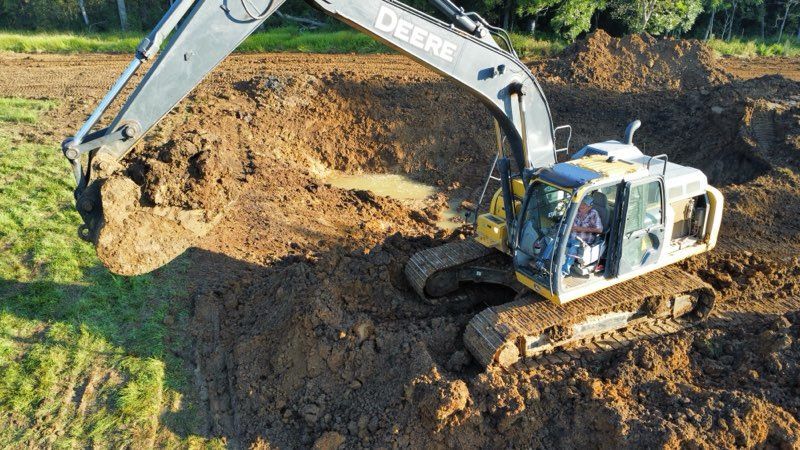 White excavator digging a large dirt mound at a construction site.