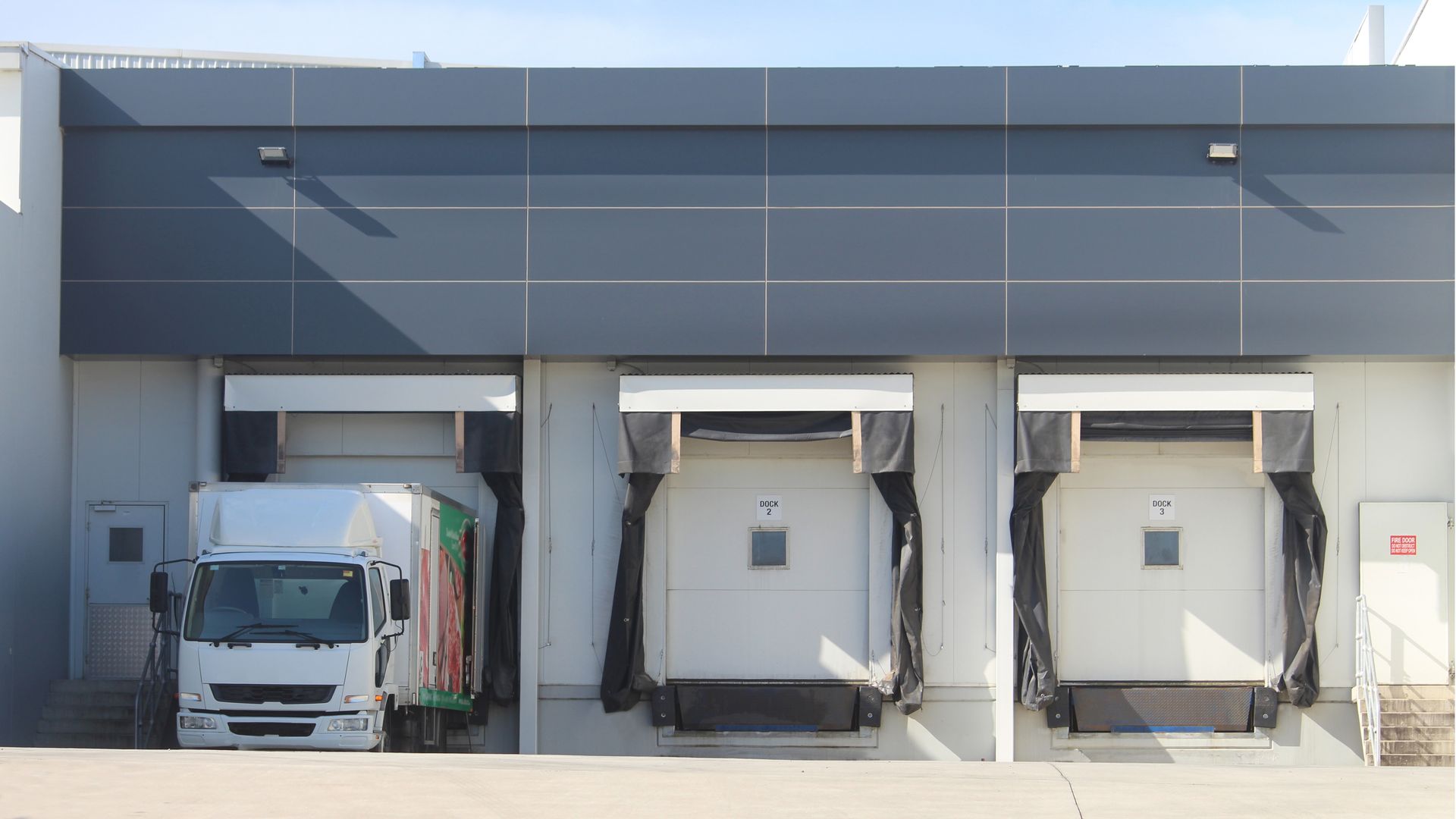 THREE REFRIGERATED TRUCK LOADING DOCKS OF A MODERN FOOD MANUFACTURING FACILITY WITH A PARKED TRUCK.