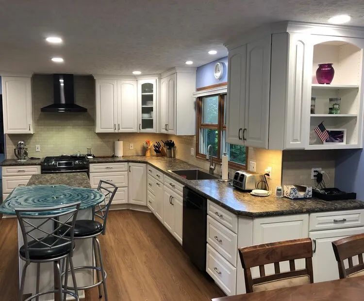 White kitchen with granite countertops, wooden floors, and stainless steel appliances.