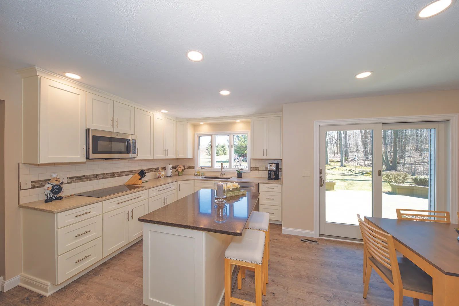 Modern kitchen with cream cabinets, brown countertops, and an island with stools, open to a backyard.