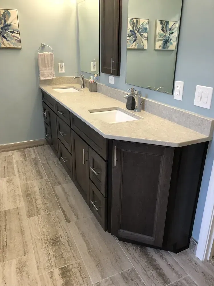 Bathroom with gray cabinets, a light countertop, two sinks, and wood-look tile flooring.