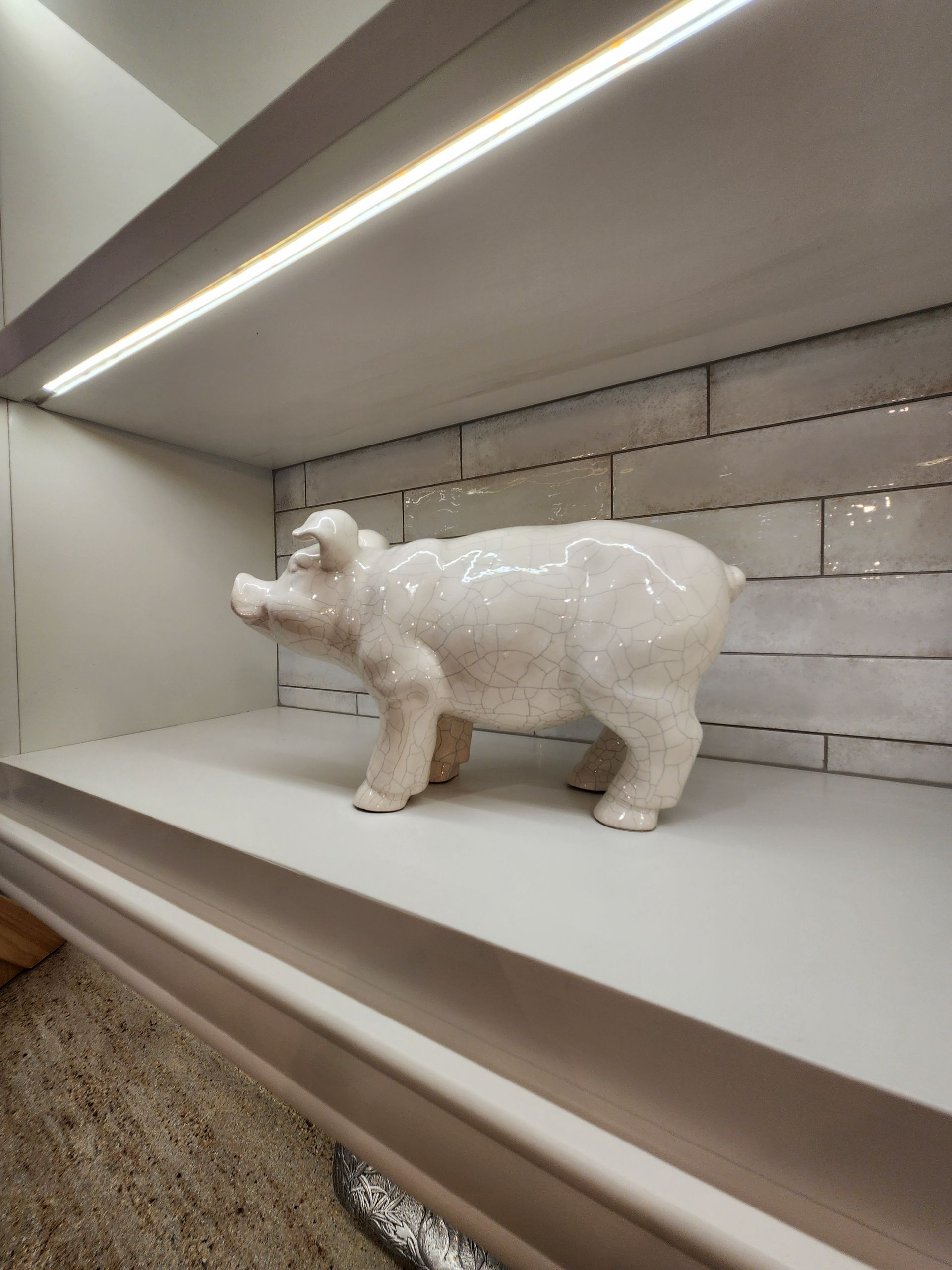 White ceramic pig on a shelf, lit by a strip light against a white brick wall.