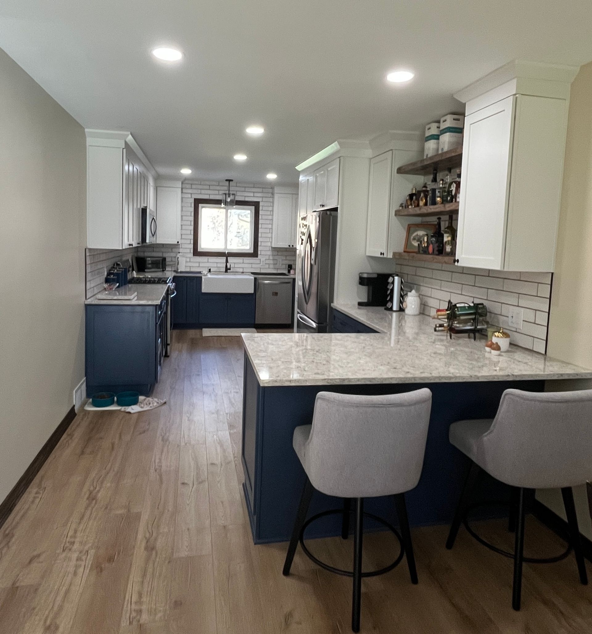 Kitchen with blue and white cabinets, granite countertops, wood floors, and two bar stools.