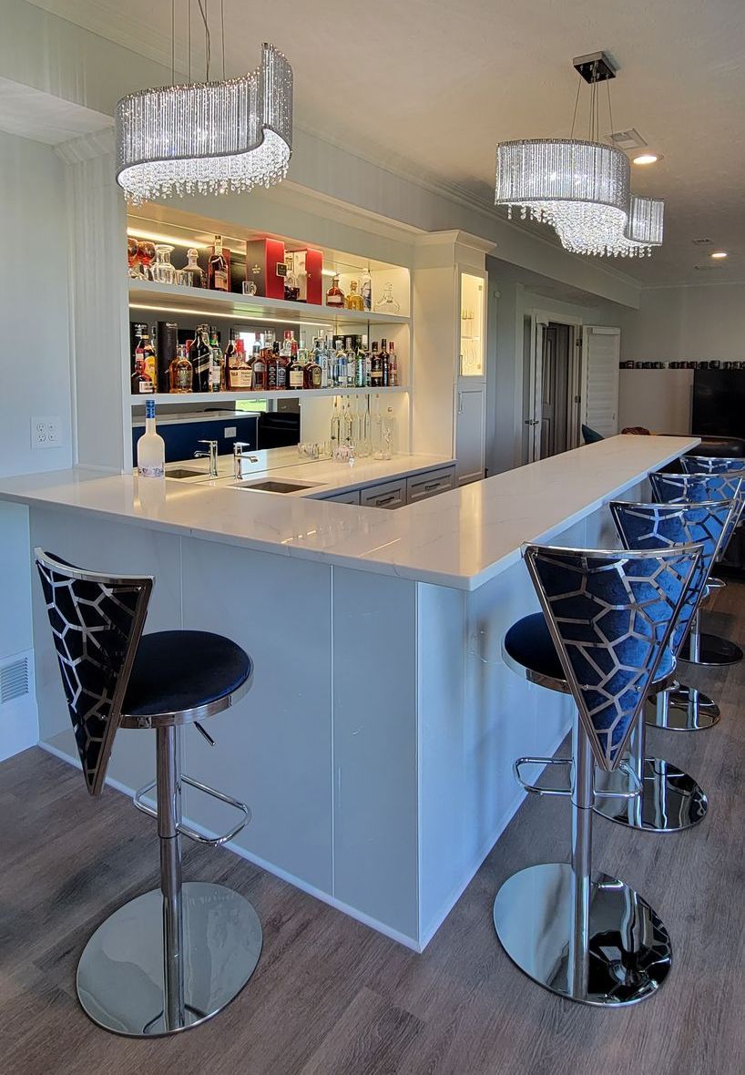 Bar with white countertop, chrome stools, and illuminated liquor shelves.