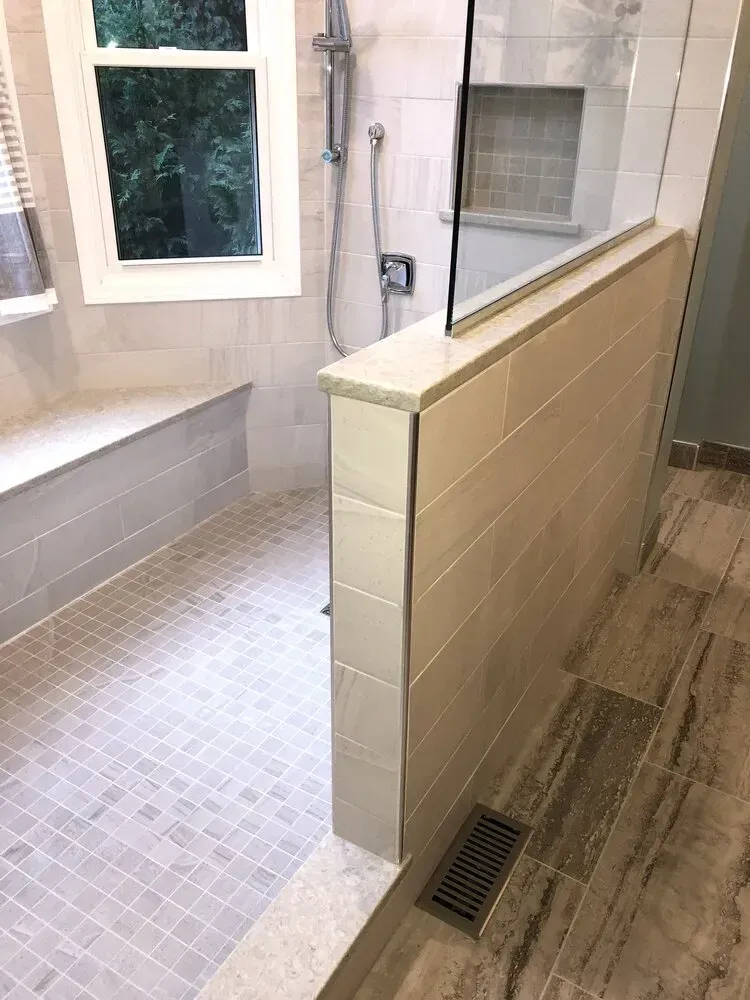 Modern bathroom with tiled shower stall, bench, and half wall.
