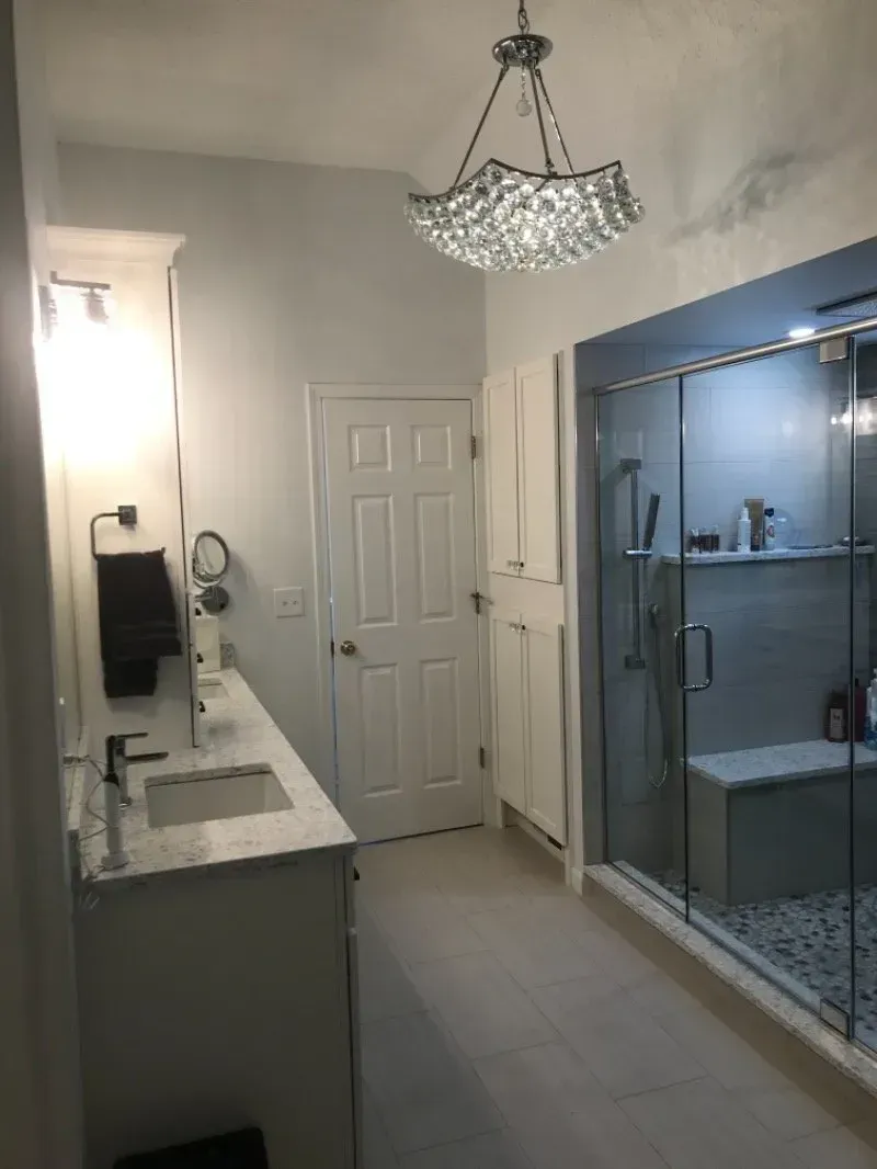 Bathroom with a white vanity, shower with glass door, and a decorative light fixture.