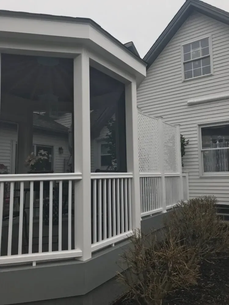 White screened-in porch with railing attached to a white house with gray foundation.