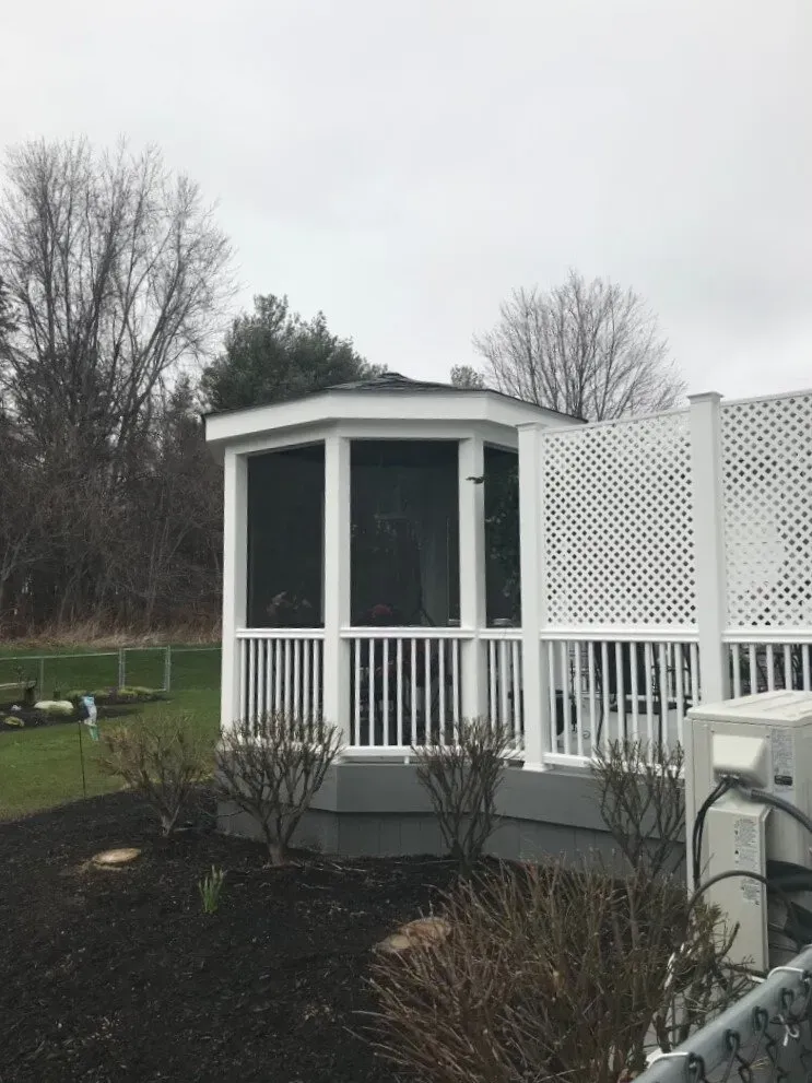 White screened-in gazebo with a gray foundation and a lattice fence. The gazebo has a black screen and white trim.