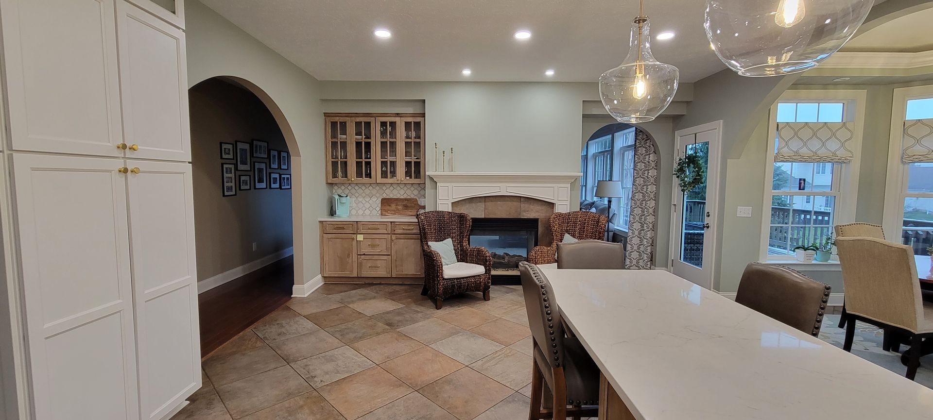 Kitchen with island, fireplace, and arched doorway, neutral tones, light fixtures.