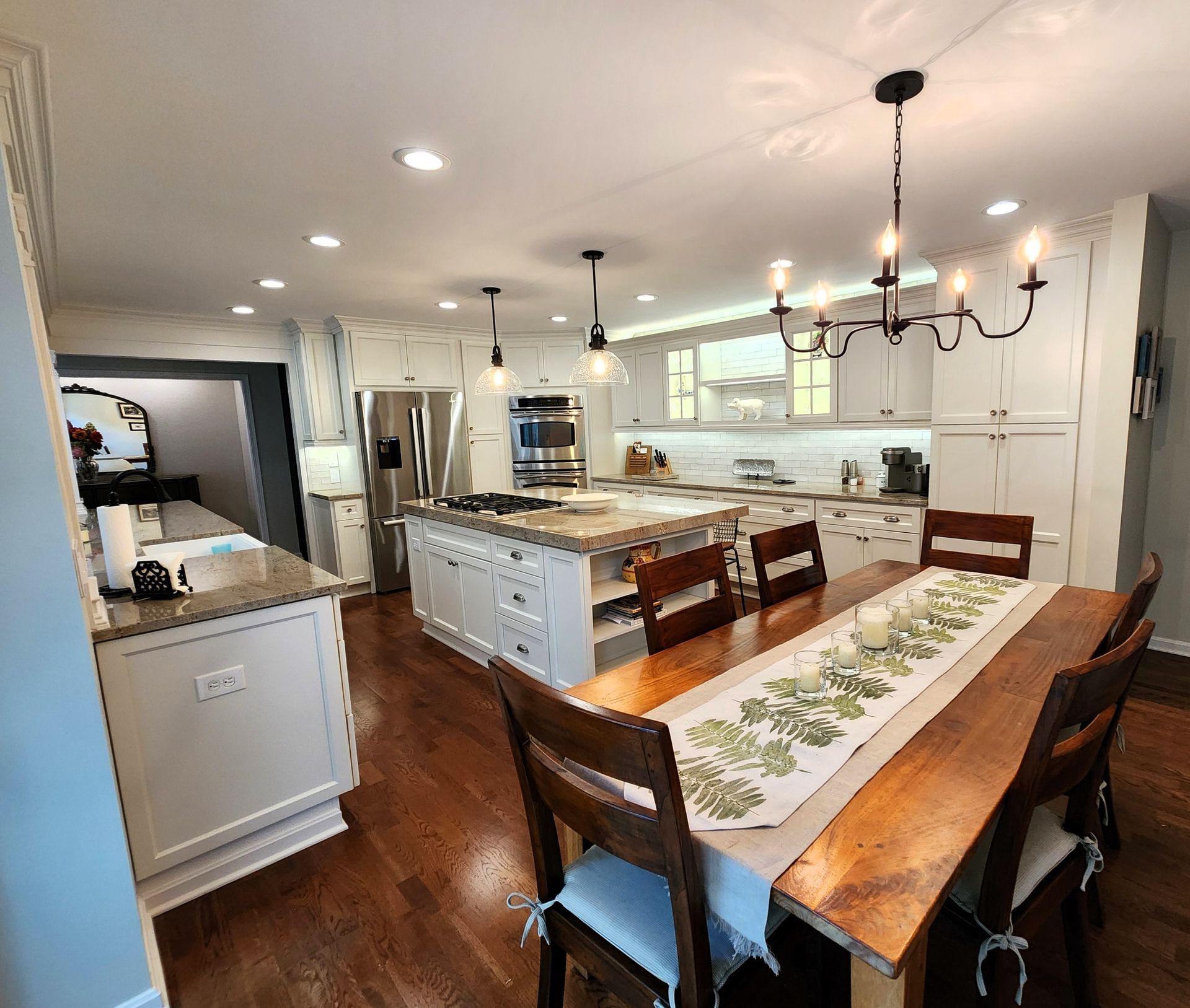Spacious kitchen with wood floors, island, and dining table; white cabinets, stainless steel appliances, and a chandelier.