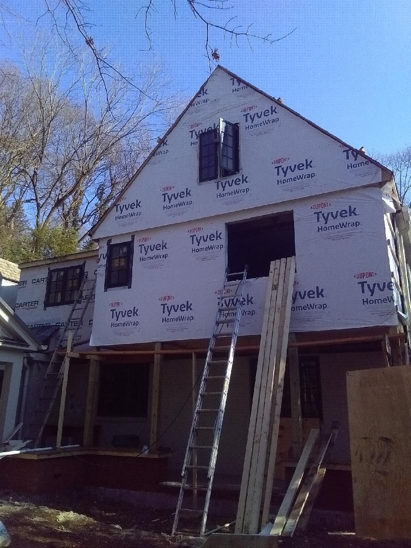 House under construction, exterior wrapped in white Tyvek, with multiple window openings and ladders.
