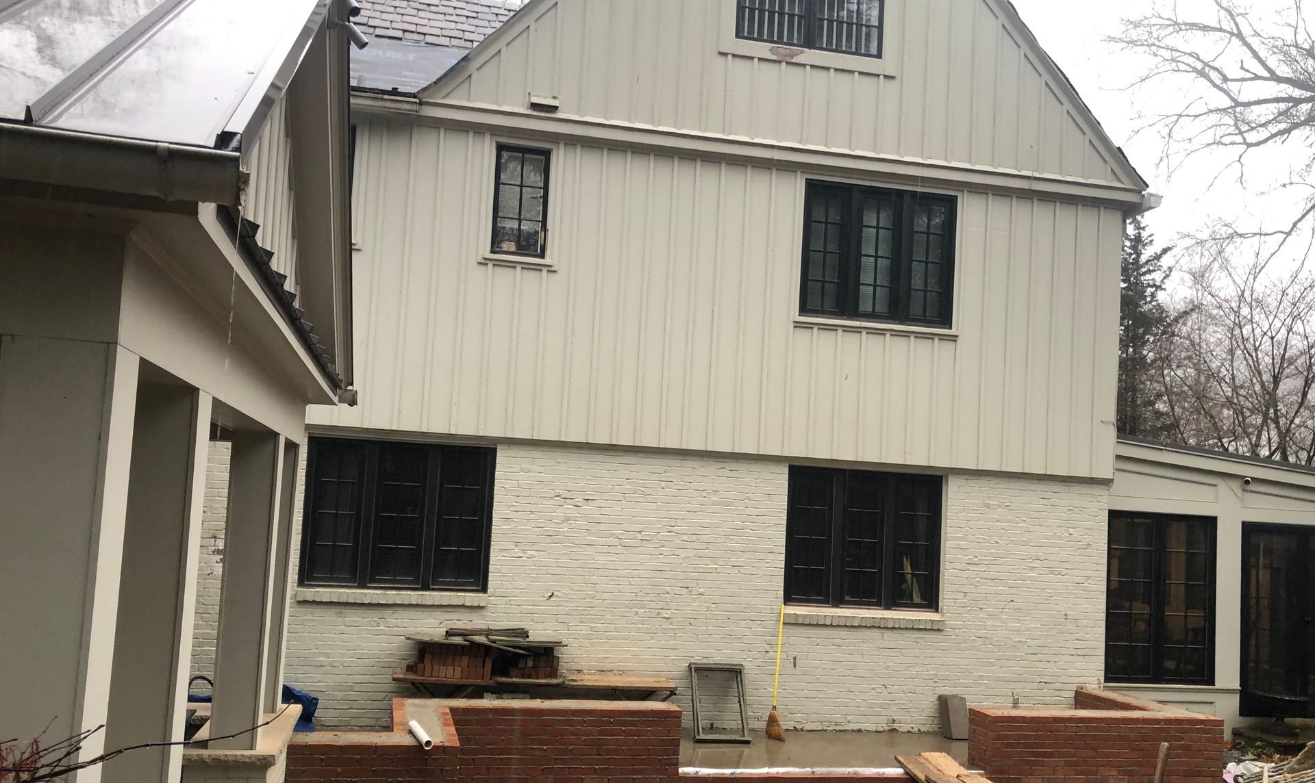 Back of a two-story beige house with black shutters, visible from a brick patio.