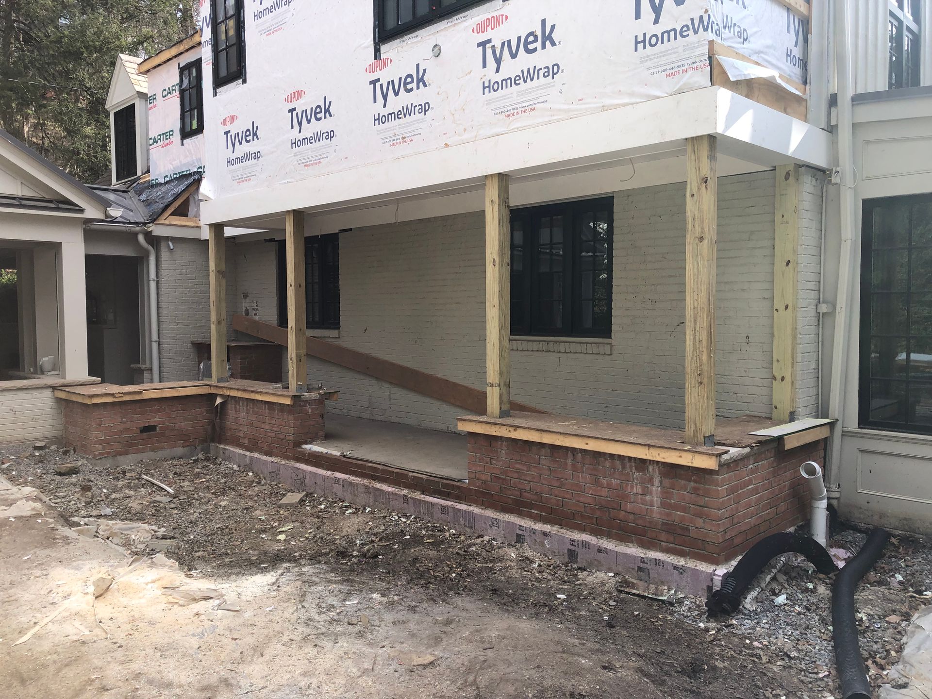 Construction of a house with a porch. White siding, wood posts, and brick base. Exterior view.