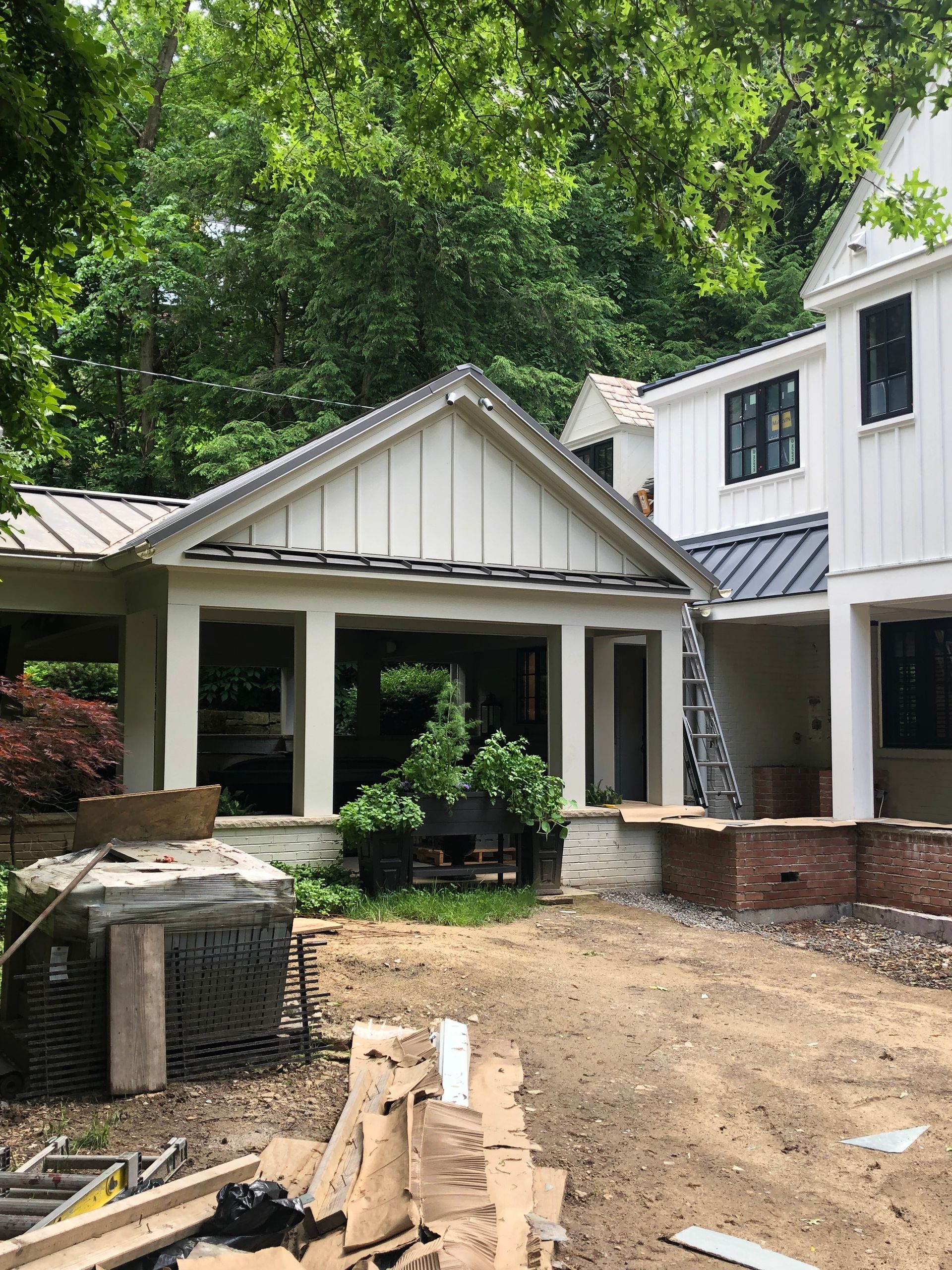 A house under construction with white siding, dark trim, and a dirt yard.
