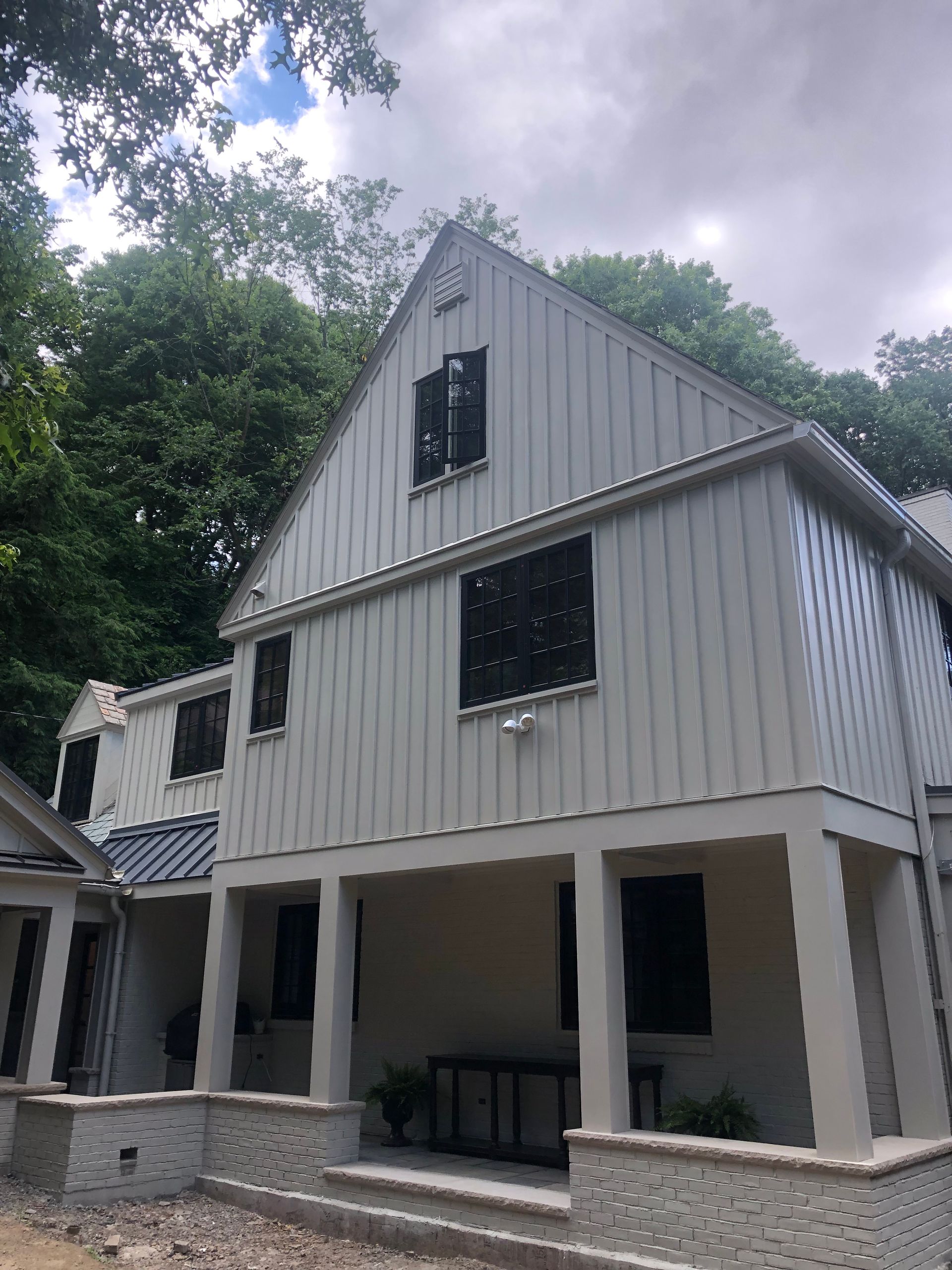 Two-story house with white siding and dark windows, set against a backdrop of trees.