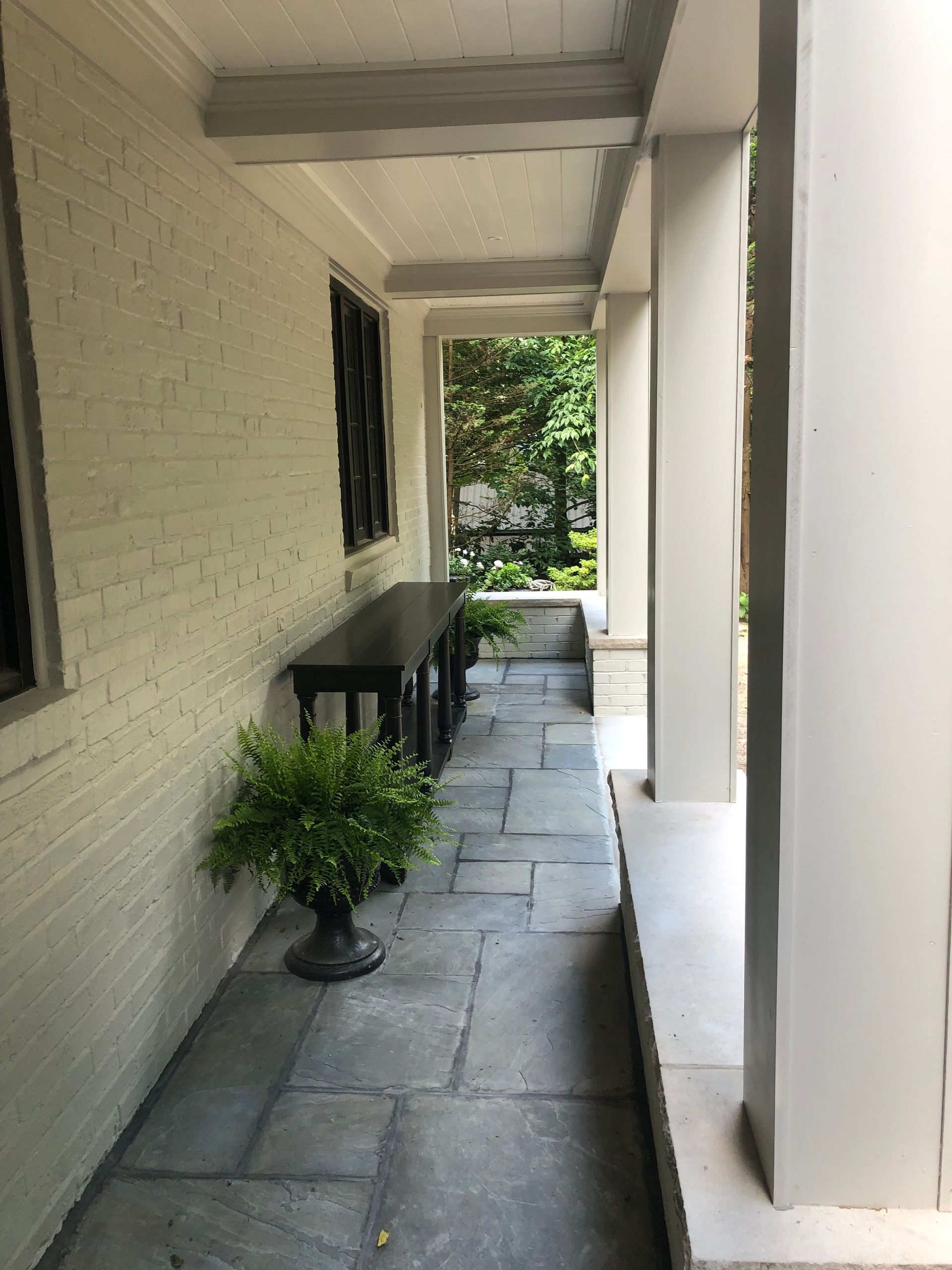 Covered porch with gray stone floor, painted brick wall, and dark table.