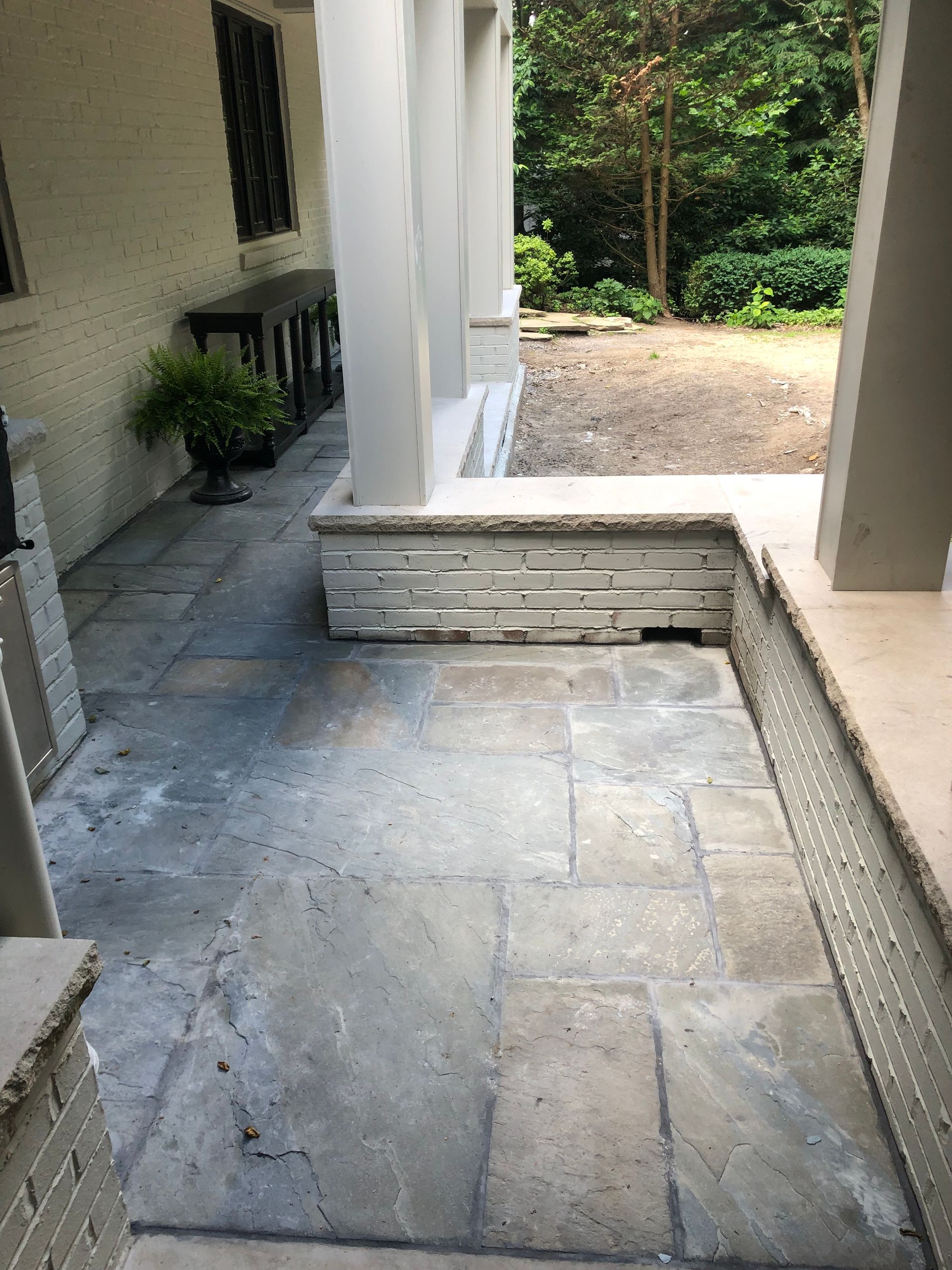 Stone patio with columns, stone wall, and greenery.