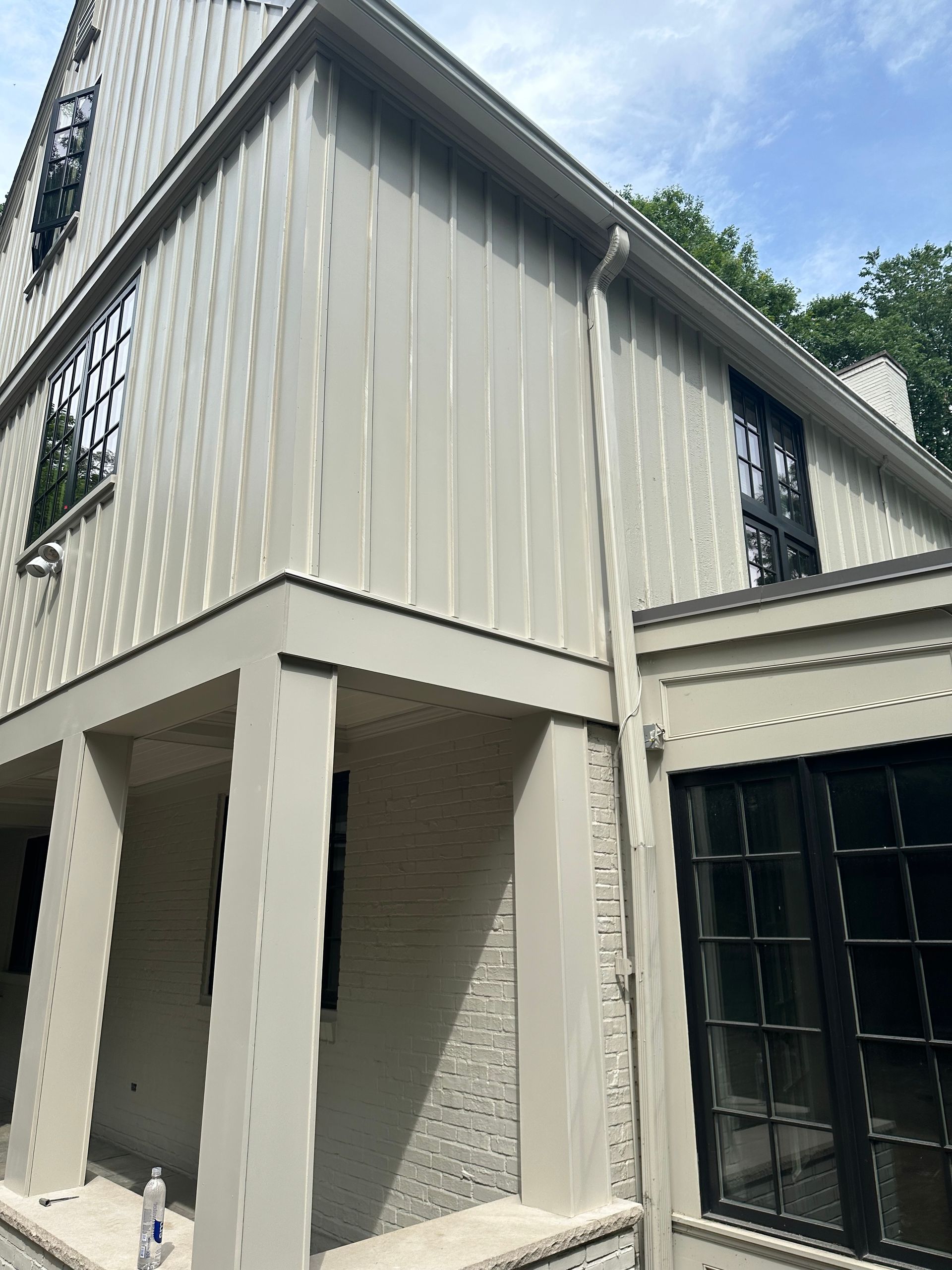 Exterior of a two-story house with light beige siding and black window frames.
