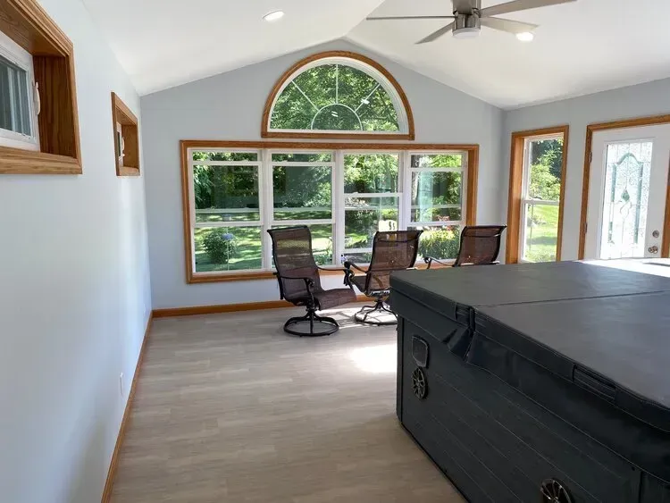 Sunroom with large windows, light blue walls, tan floor, hot tub, and patio chairs.