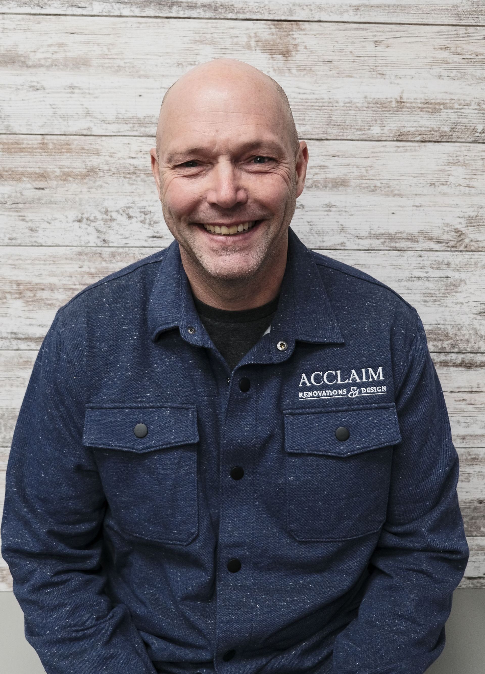 Bald man smiling, wearing a blue button-up shirt with 
