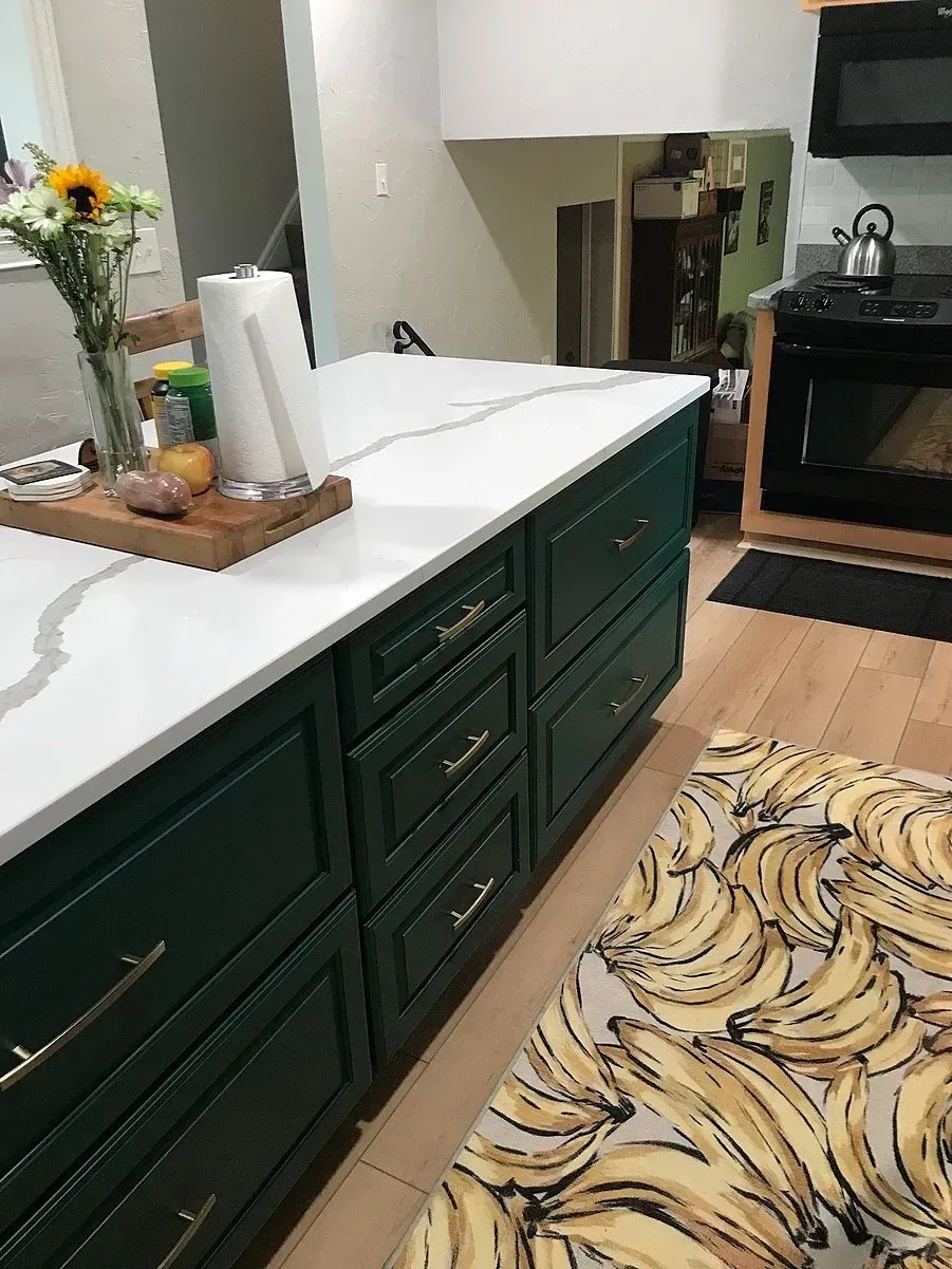 Green kitchen island with white countertop. Flowers and paper towels sit atop the island.